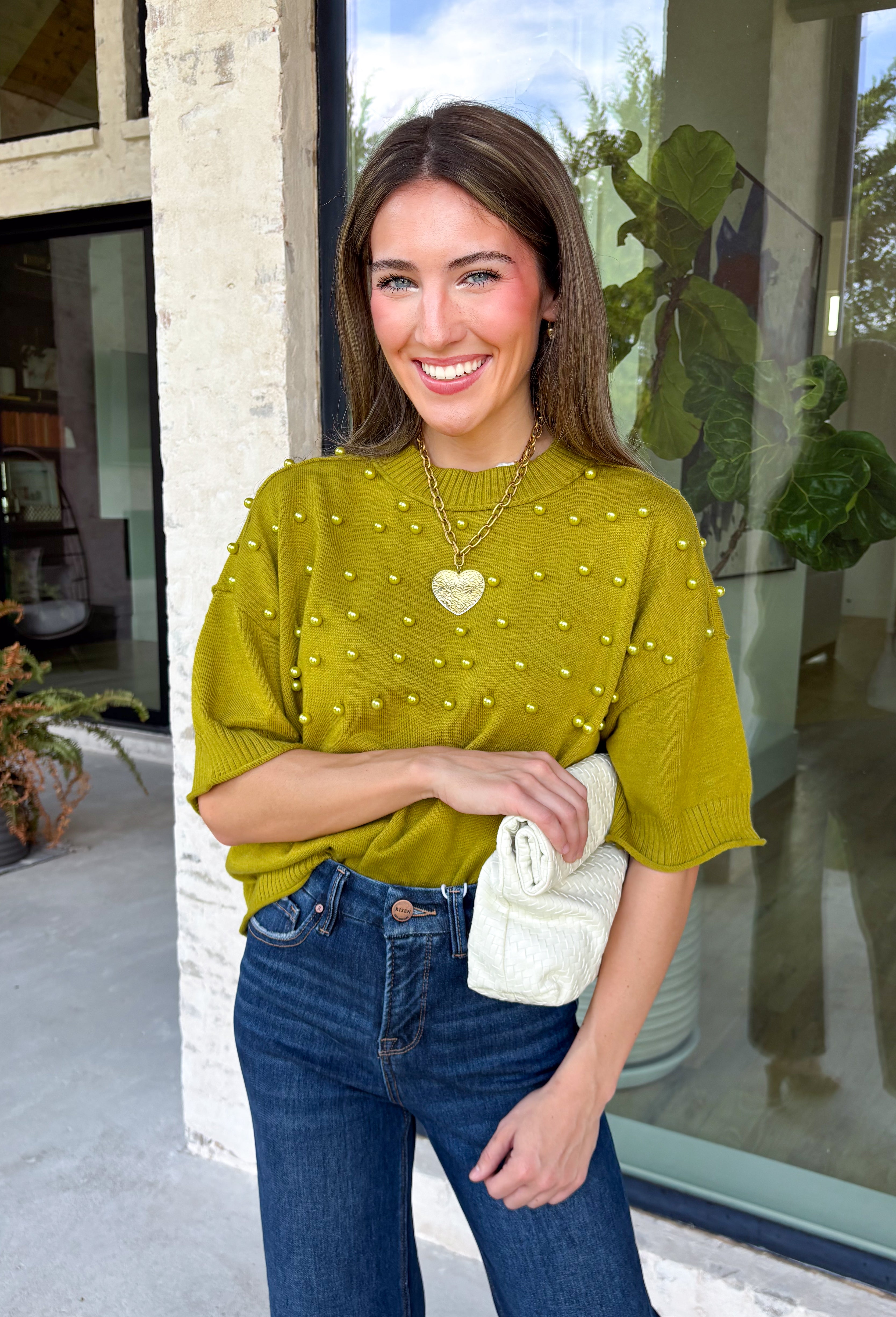 A rich olive green gets a pretty update with this pearl-detailed short sleeve sweater from Glam. Pearl detailing throughout adds a special touch to the soft knit, making it easy to dress up while still keeping that cozy, everyday feel. Exposed hems bring in a relaxed finish, while ribbed detailing along the neckline, sleeve cuffs, and hem gives it a classic sweater look. Wear it to the office, dinner plans, or anytime your outfit could use a little something extra.