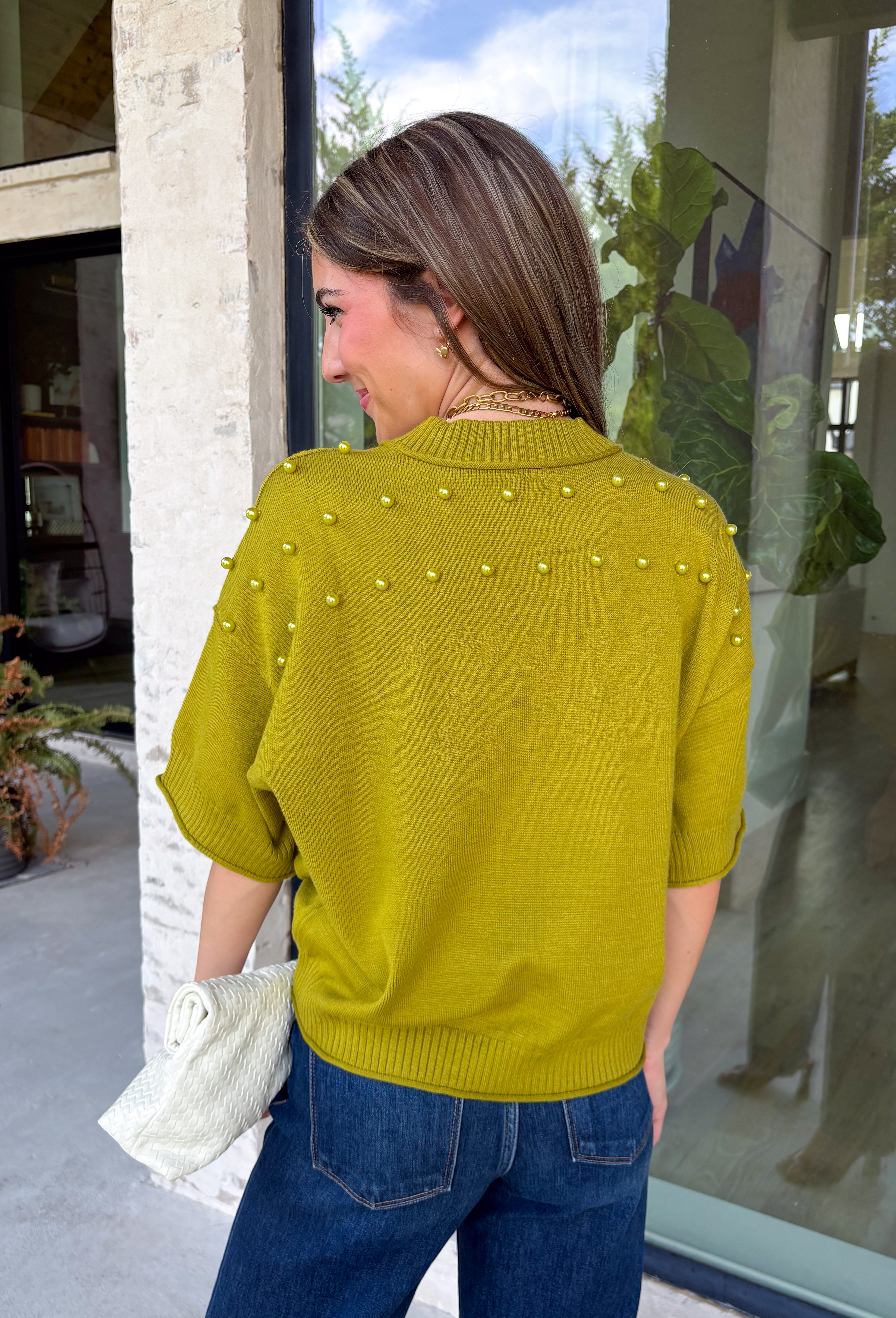 A rich olive green gets a pretty update with this pearl-detailed short sleeve sweater from Glam. Pearl detailing throughout adds a special touch to the soft knit, making it easy to dress up while still keeping that cozy, everyday feel. Exposed hems bring in a relaxed finish, while ribbed detailing along the neckline, sleeve cuffs, and hem gives it a classic sweater look. Wear it to the office, dinner plans, or anytime your outfit could use a little something extra.