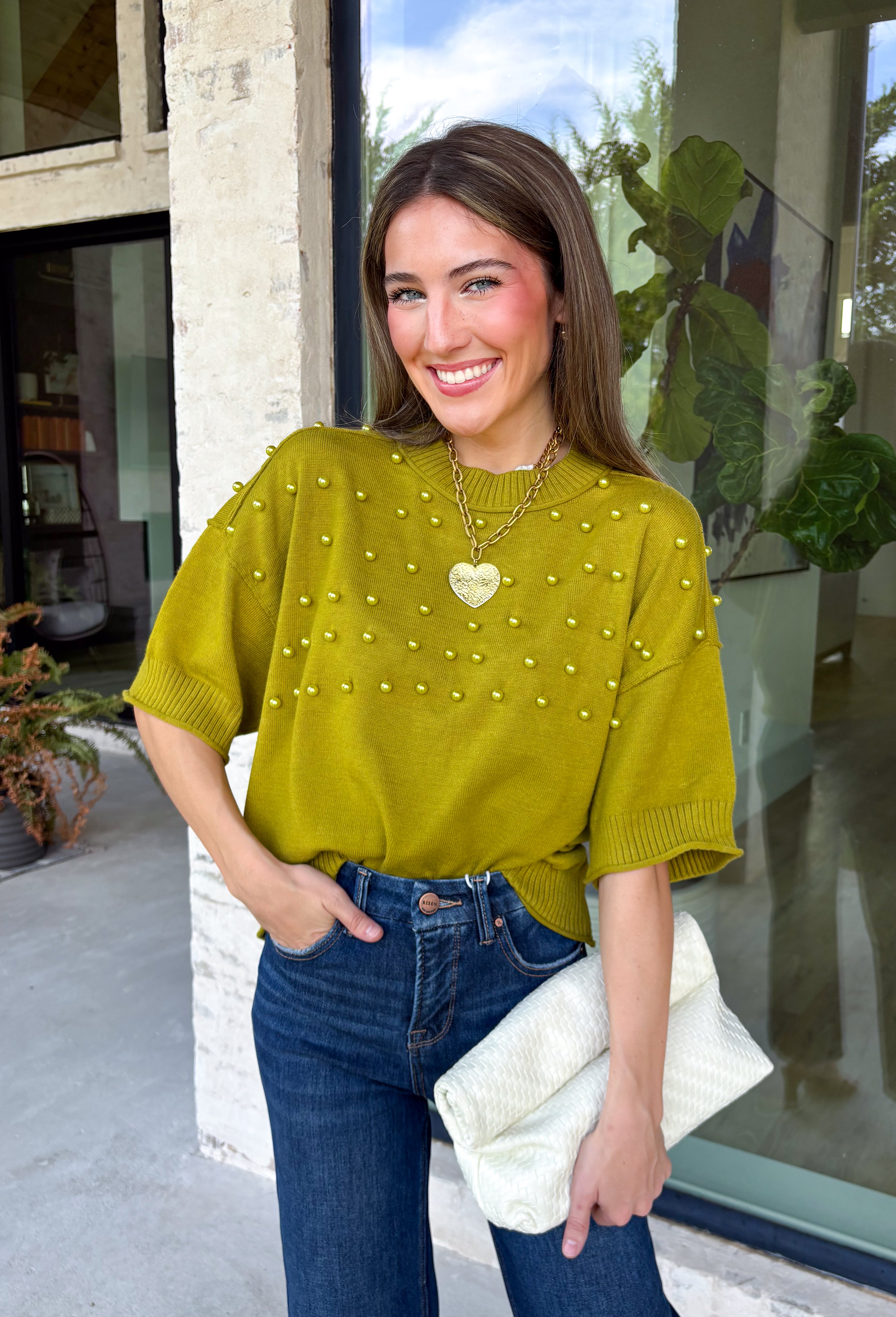 A rich olive green gets a pretty update with this pearl-detailed short sleeve sweater from Glam. Pearl detailing throughout adds a special touch to the soft knit, making it easy to dress up while still keeping that cozy, everyday feel. Exposed hems bring in a relaxed finish, while ribbed detailing along the neckline, sleeve cuffs, and hem gives it a classic sweater look. Wear it to the office, dinner plans, or anytime your outfit could use a little something extra.
