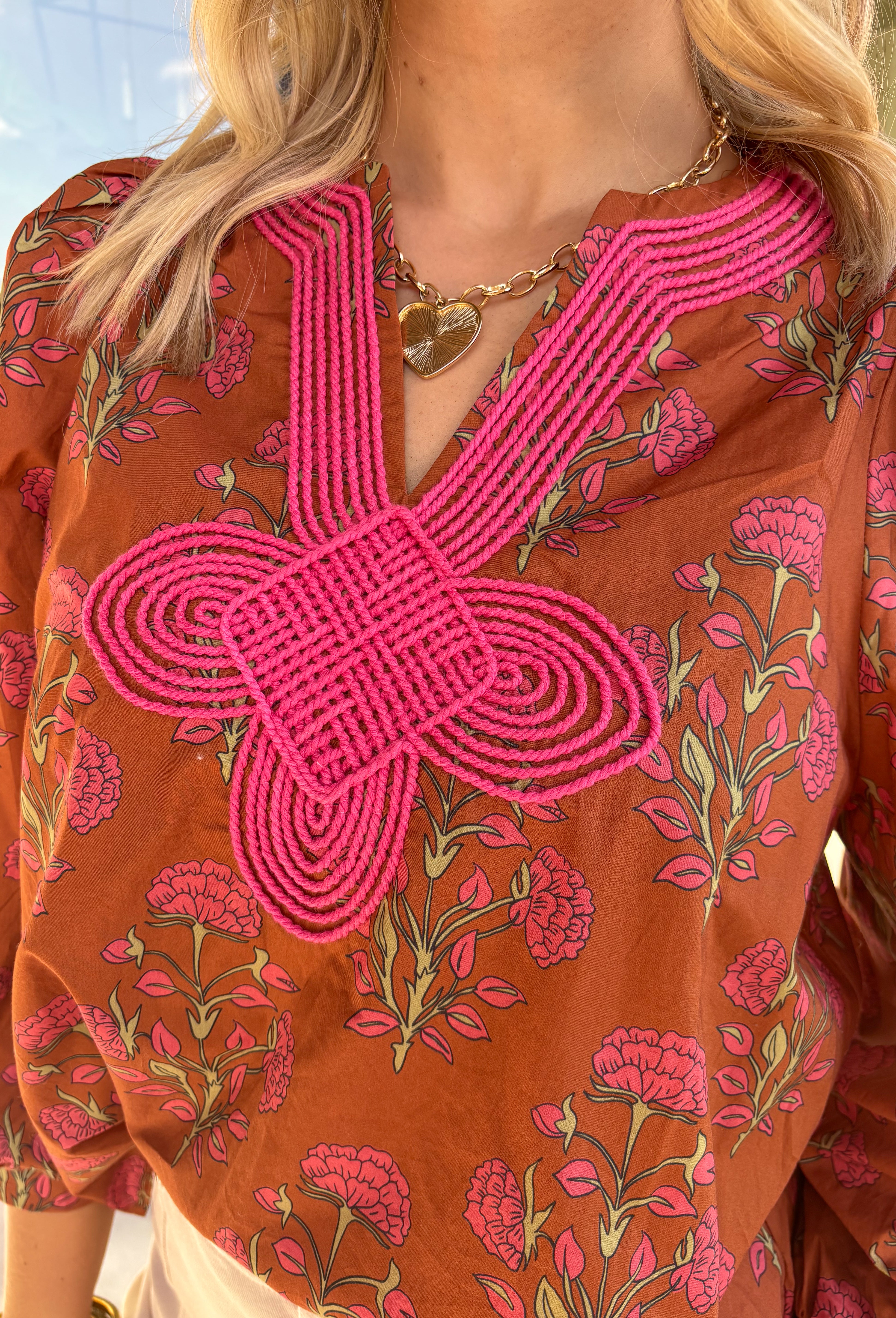 Bring a soft, romantic touch to your winter wardrobe with this floral puff sleeve top by Entro. Designed in a warm brown base with a pink floral print, this top features a contrast embroidered knot trim that outlines the v-neck for an extra hint of detail. The long puff sleeves add a feminine finish, making it perfect for cozy days that still call for a polished look.