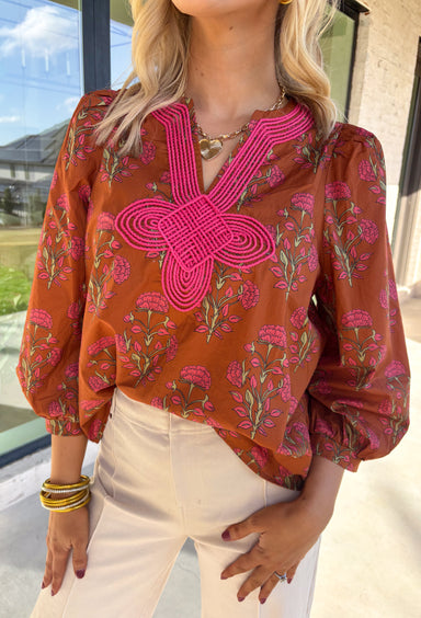 Bring a soft, romantic touch to your winter wardrobe with this floral puff sleeve top by Entro. Designed in a warm brown base with a pink floral print, this top features a contrast embroidered knot trim that outlines the v-neck for an extra hint of detail. The long puff sleeves add a feminine finish, making it perfect for cozy days that still call for a polished look.