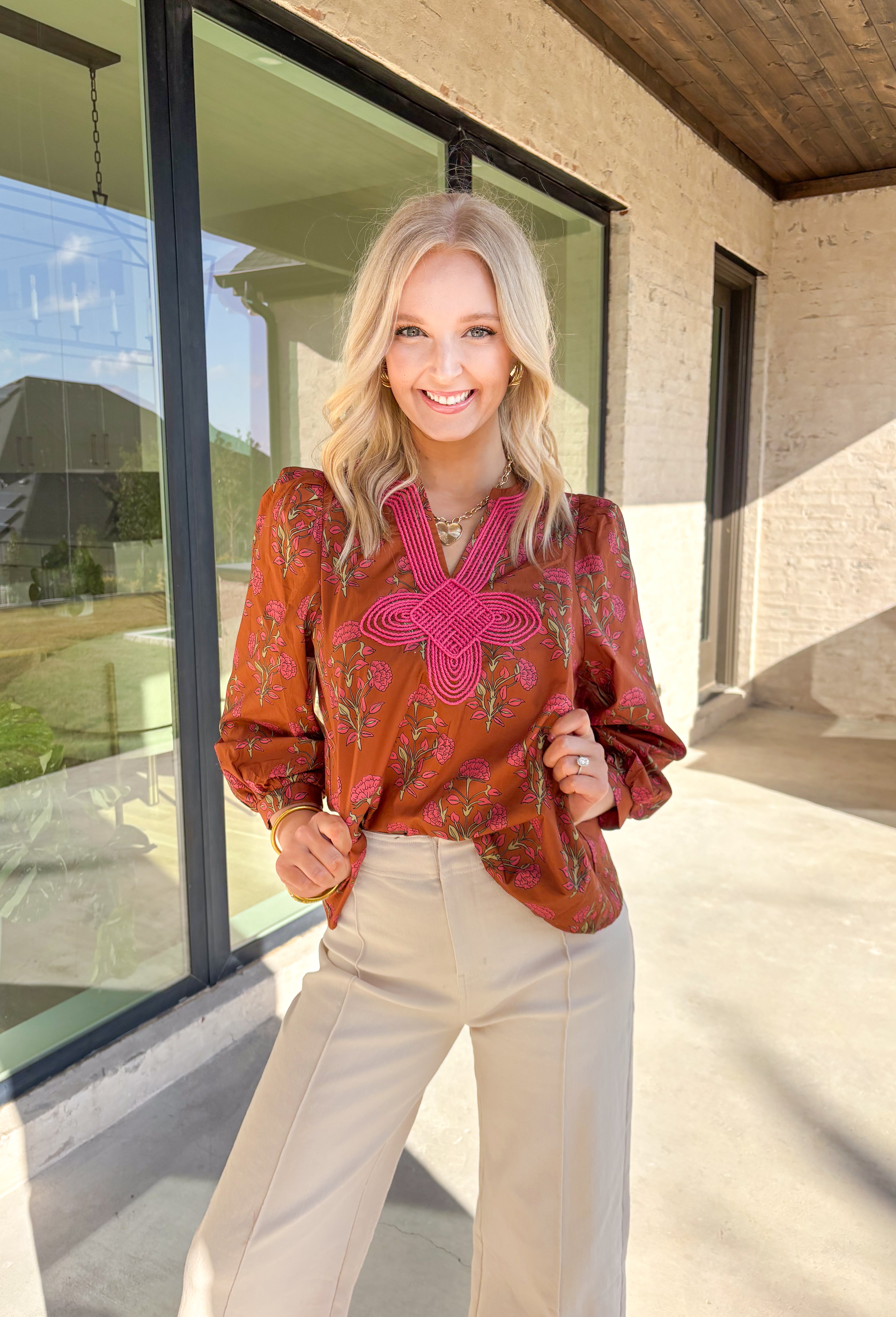 Bring a soft, romantic touch to your winter wardrobe with this floral puff sleeve top by Entro. Designed in a warm brown base with a pink floral print, this top features a contrast embroidered knot trim that outlines the v-neck for an extra hint of detail. The long puff sleeves add a feminine finish, making it perfect for cozy days that still call for a polished look.