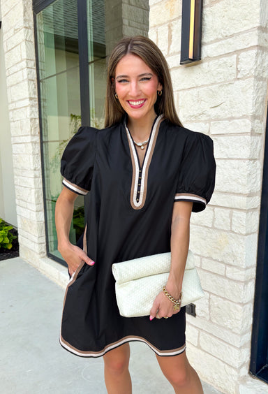Classic with a modern twist, this black dress is the definition of effortless fall style. Classic black is beautifully accented with tan and cream trim along the front, sides, hem, and sleeves for a look that feels both timeless and eye-catching. The front button details and soft puff sleeves add just the right amount of charm, while the fully lined design and side pockets make it as comfortable as it is stylish. 