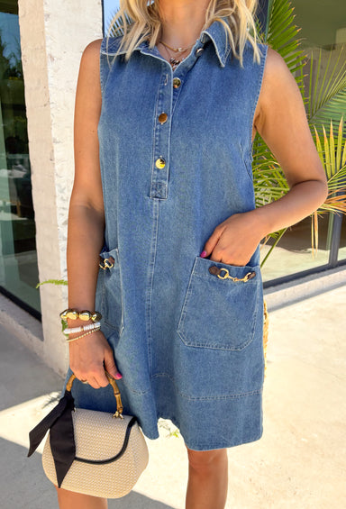 This sleeveless denim mini dress is the perfect mix of classic and cool for summer. Designed with a button front and front flap pockets featuring buckle accents, it brings a subtle utility vibe that feels both trendy and timeless. The lightweight cotton keeps it breathable for warm days, while the structured shape makes it easy to dress up or down. Whether you're heading to brunch, running errands, or packing for vacation, this is one of those throw-on-and-go pieces that always works. 
