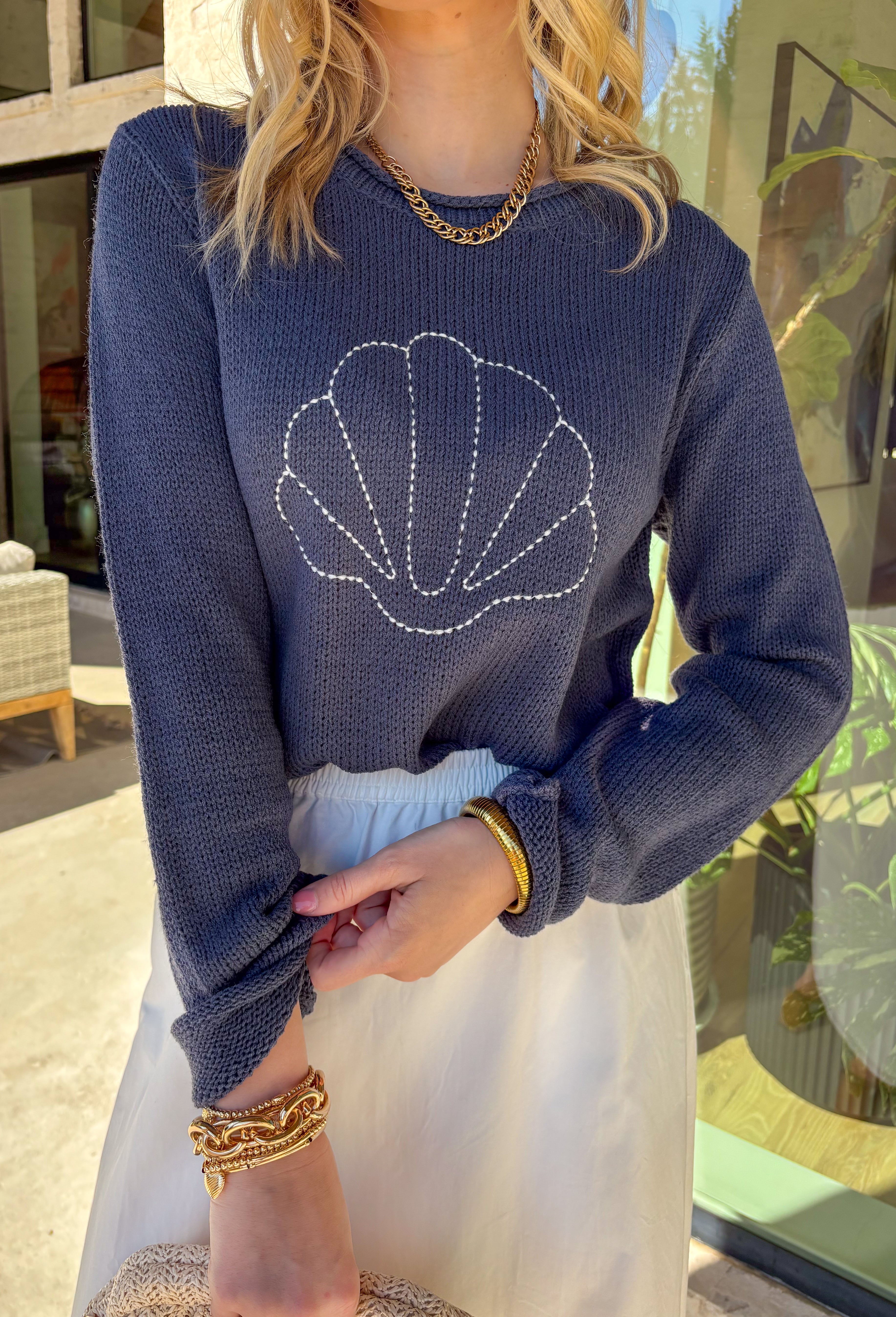 This navy lightweight knit sweater is giving effortless coastal vibes in the cutest way! Featuring a white seashell embroidered print across the front, it adds the perfect playful detail without being too loud. The soft knit feel makes it easy to toss on for breezy spring days, chilly beach nights, or those mornings when it’s warm in the sun but cool in the shade.