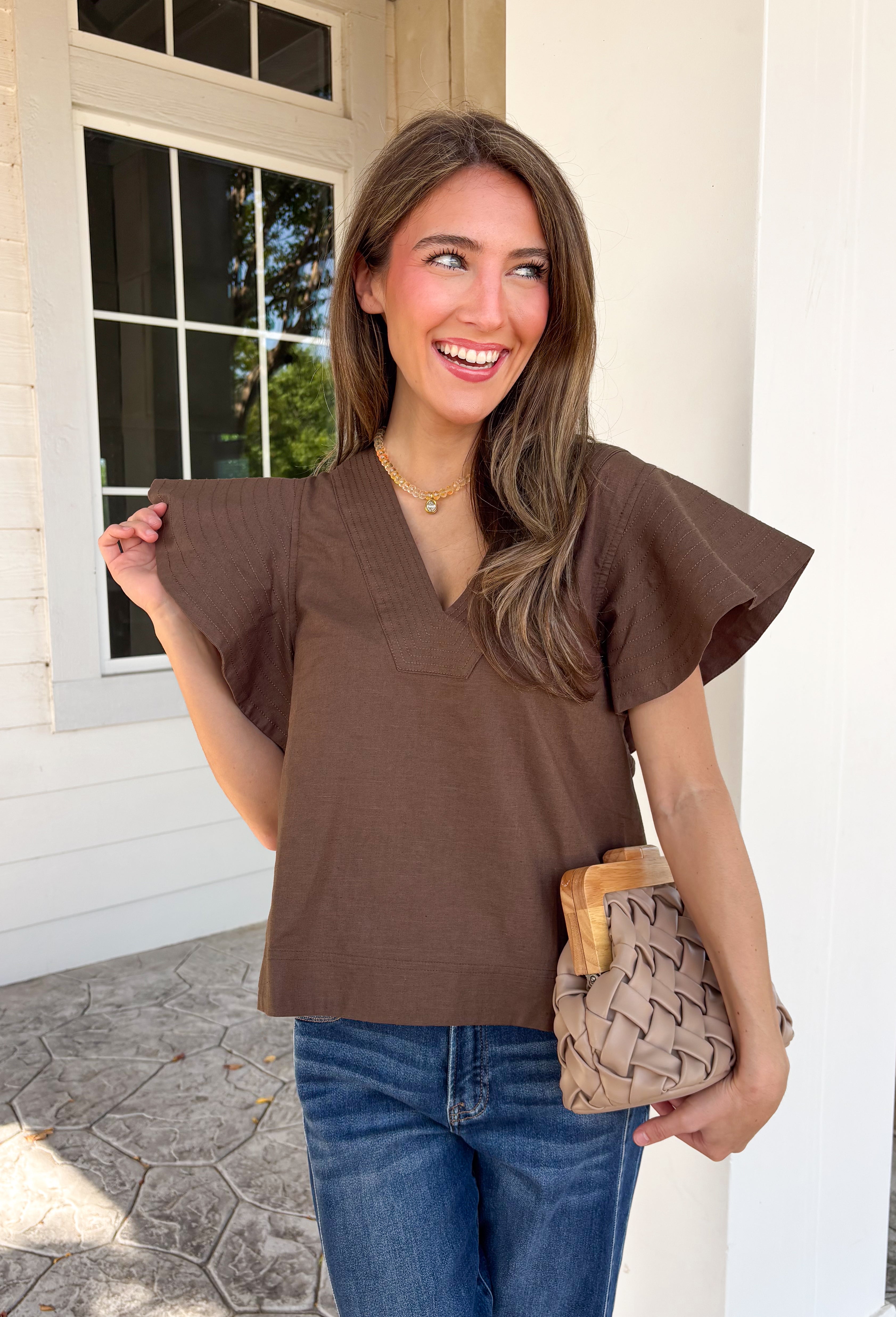 Simple details make all the difference in this effortlessly beautiful brown top! Crafted from a breathable cotton and linen blend, this timeless top is perfect for transitioning through the fall season. The flattering v-neckline is accented with delicate stitch detailing, while flutter sleeves add a soft, feminine touch. A button closure at the back completes the look with subtle charm. 