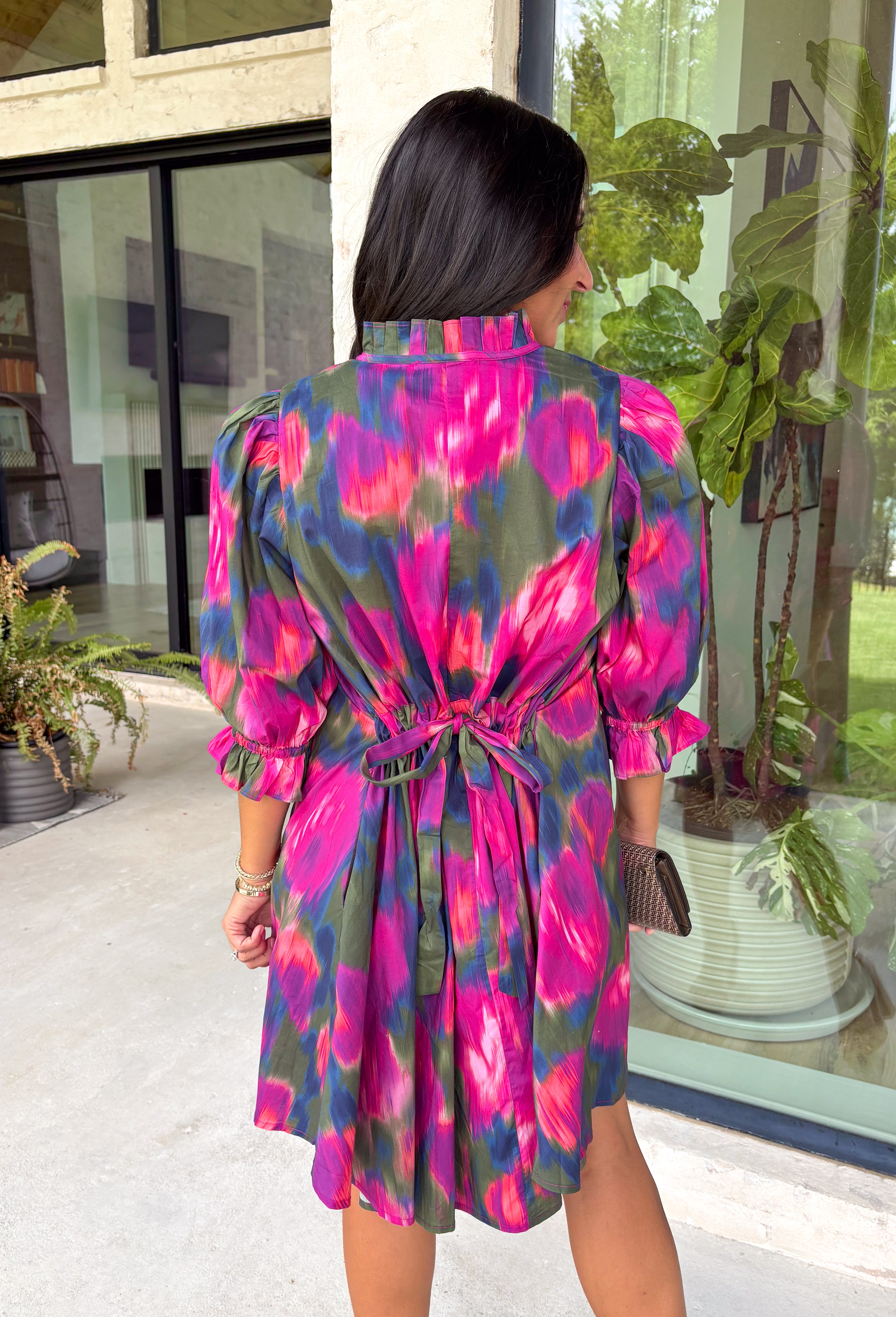 Make every occasion feel a little more special in this beautifully detailed dress from Entro. Featuring a stunning abstract print in rich shades of magenta, olive, navy, and pink, this feminine dress is full of eye-catching seasonal color. The ruffled mock neckline and button-front design create a timeless silhouette, while the matching self-tie belt flatters your waist for a customizable fit. Puff sleeves with elastic ruffle cuffs add a sweet finishing touch, and side pockets make it as practical.