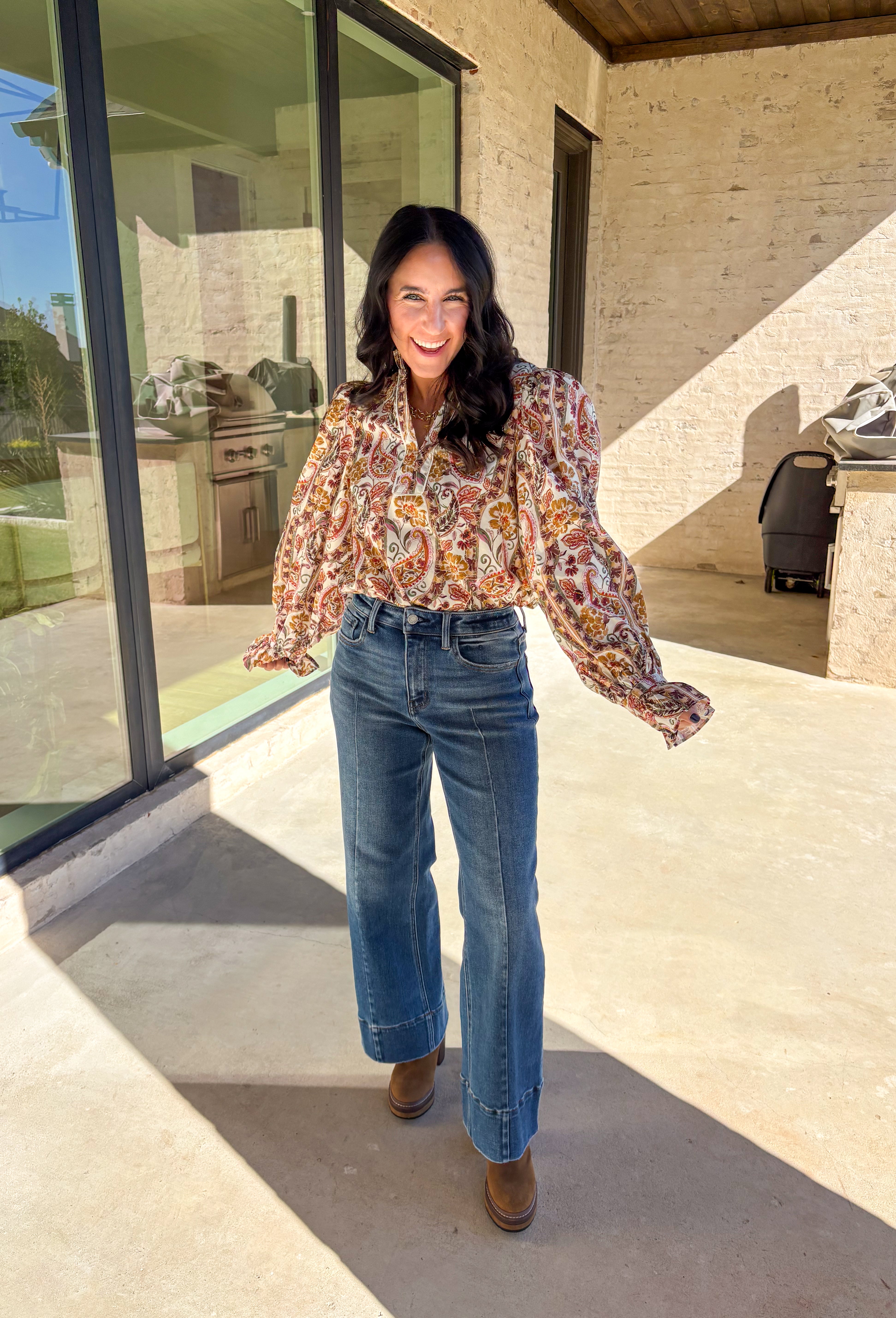 Effortlessly feminine and fall-ready, this neutral paisley print top by Entro brings timeless charm to your wardrobe. Designed with a ruffled band collar and a v-neckline, it offers just the right mix of structure and softness. The buttoned cuffs with delicate ruffle edges add a romantic finishing touch, making it easy to dress up or wear casually through the season.
