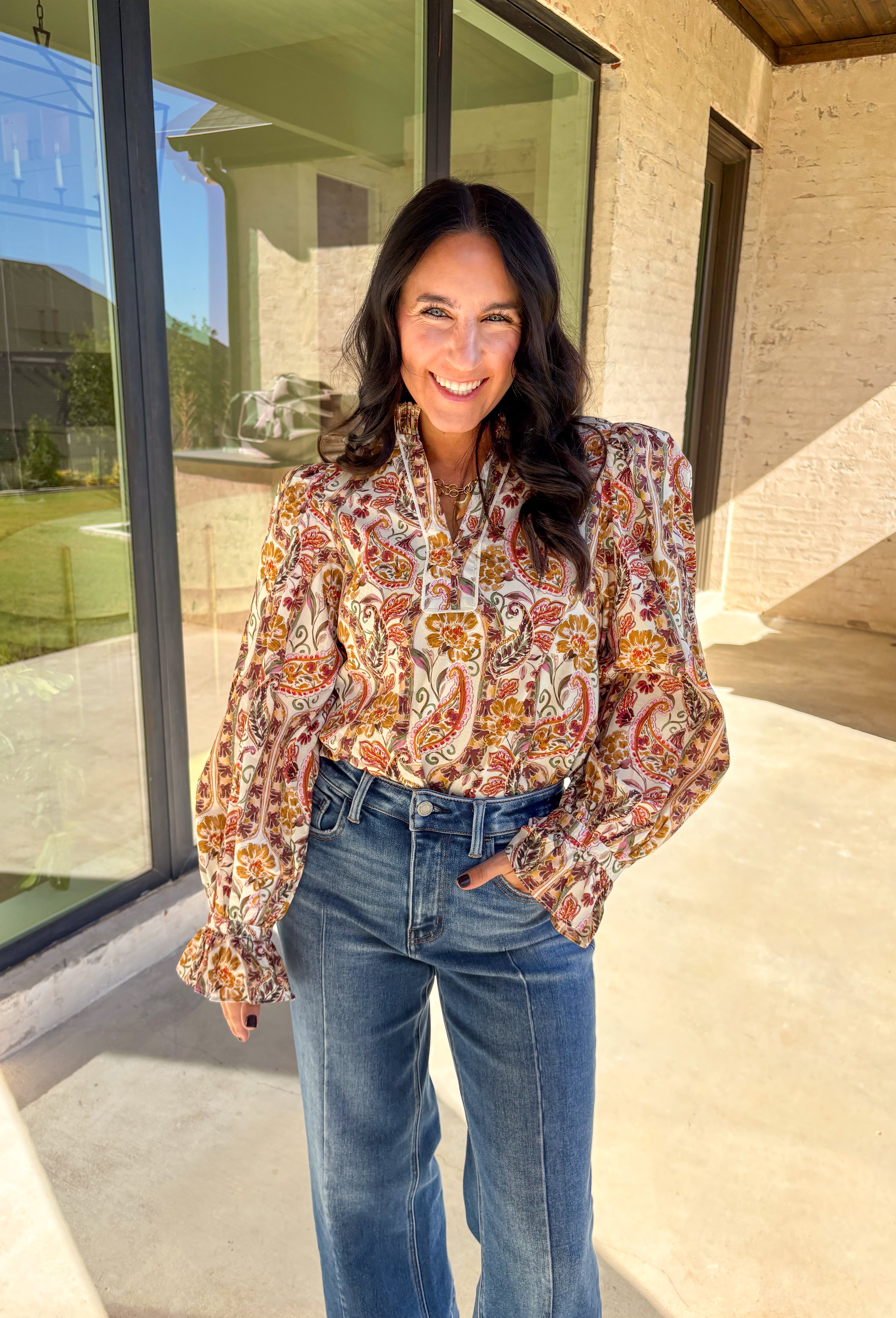 Effortlessly feminine and fall-ready, this neutral paisley print top by Entro brings timeless charm to your wardrobe. Designed with a ruffled band collar and a v-neckline, it offers just the right mix of structure and softness. The buttoned cuffs with delicate ruffle edges add a romantic finishing touch, making it easy to dress up or wear casually through the season.