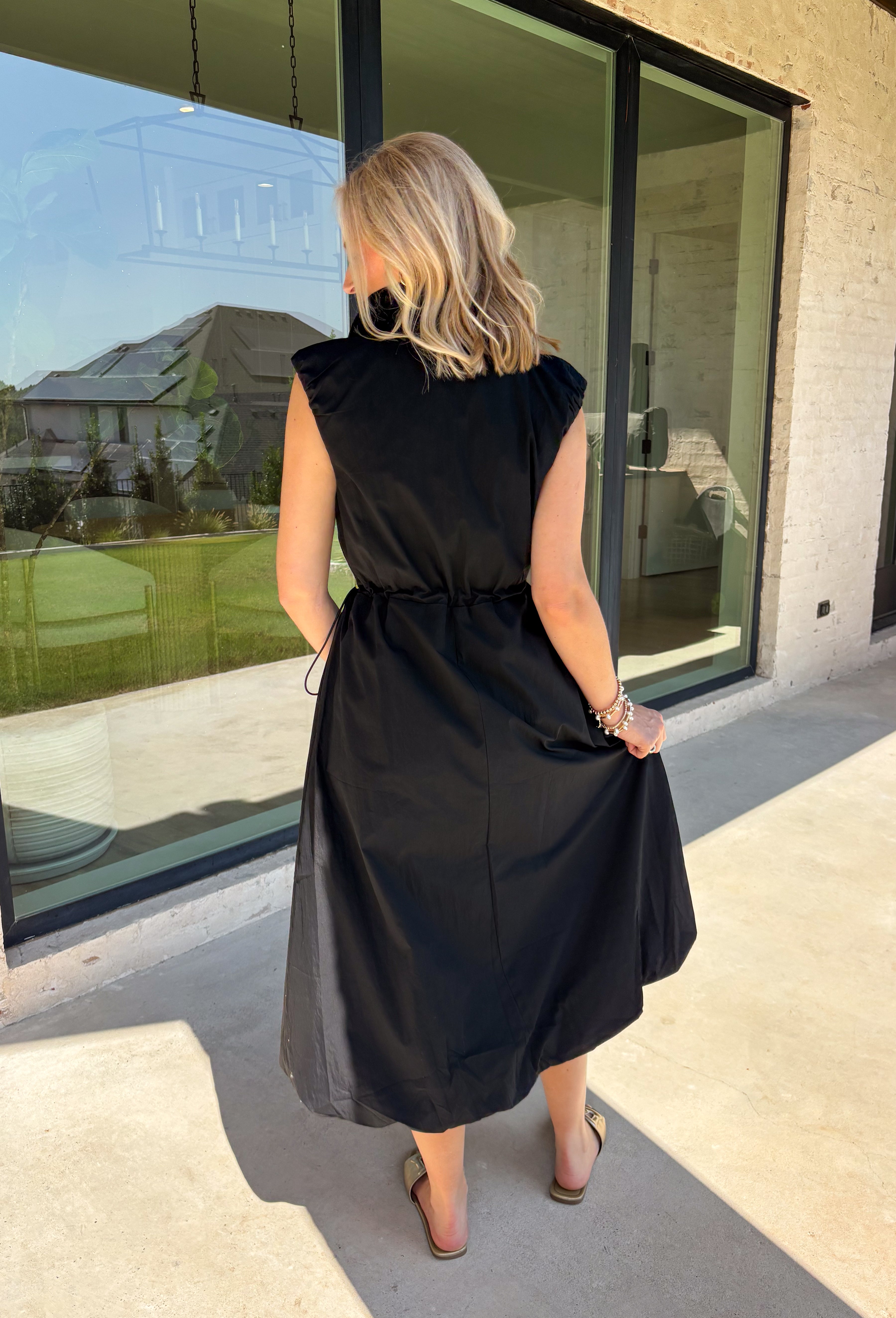 Meet your new throw-on-and-go favorite with this black utility-inspired midi dress from Entro. The classic black color keeps it versatile, while the zipper-front closure and adjustable waist give it a sporty, modern feel. A bubble hem adds shape and a fun unexpected finish, while the sleeveless silhouette makes it easy to wear now and layer as the temperatures cool down. Complete with convenient side pockets, this dress is ready for busy workdays, weekend plans, travel days, and everything in between.
