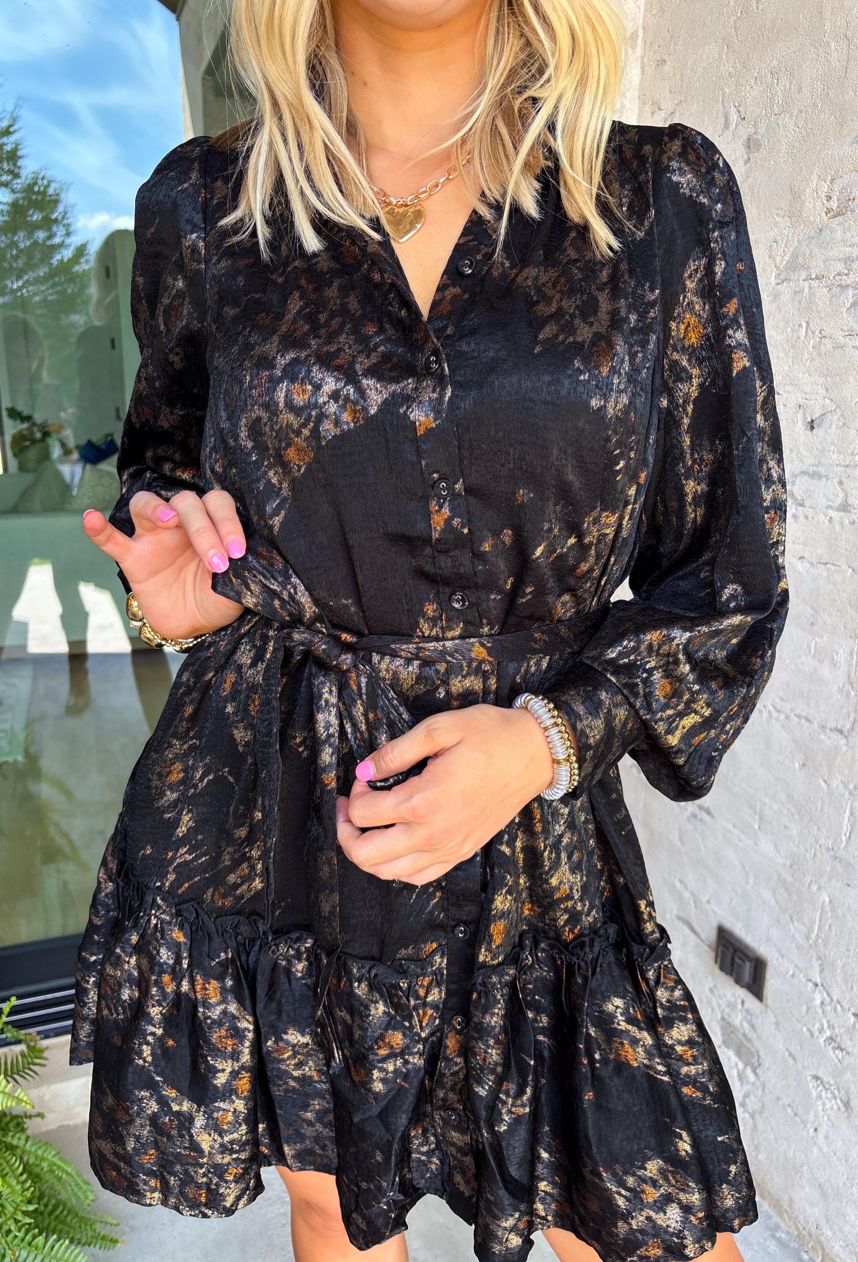 Bring a little shimmer to the season with this black long sleeve dress. Designed with a subtle leopard print in a textured, metallic-like finish, it adds depth and shine without being over the top. A button-down front and ruffle trim soften the look, making it equal parts chic and feminine. Lightweight yet lined, this dress is a perfect choice for special occasions, evening dinners, or holiday gatherings.