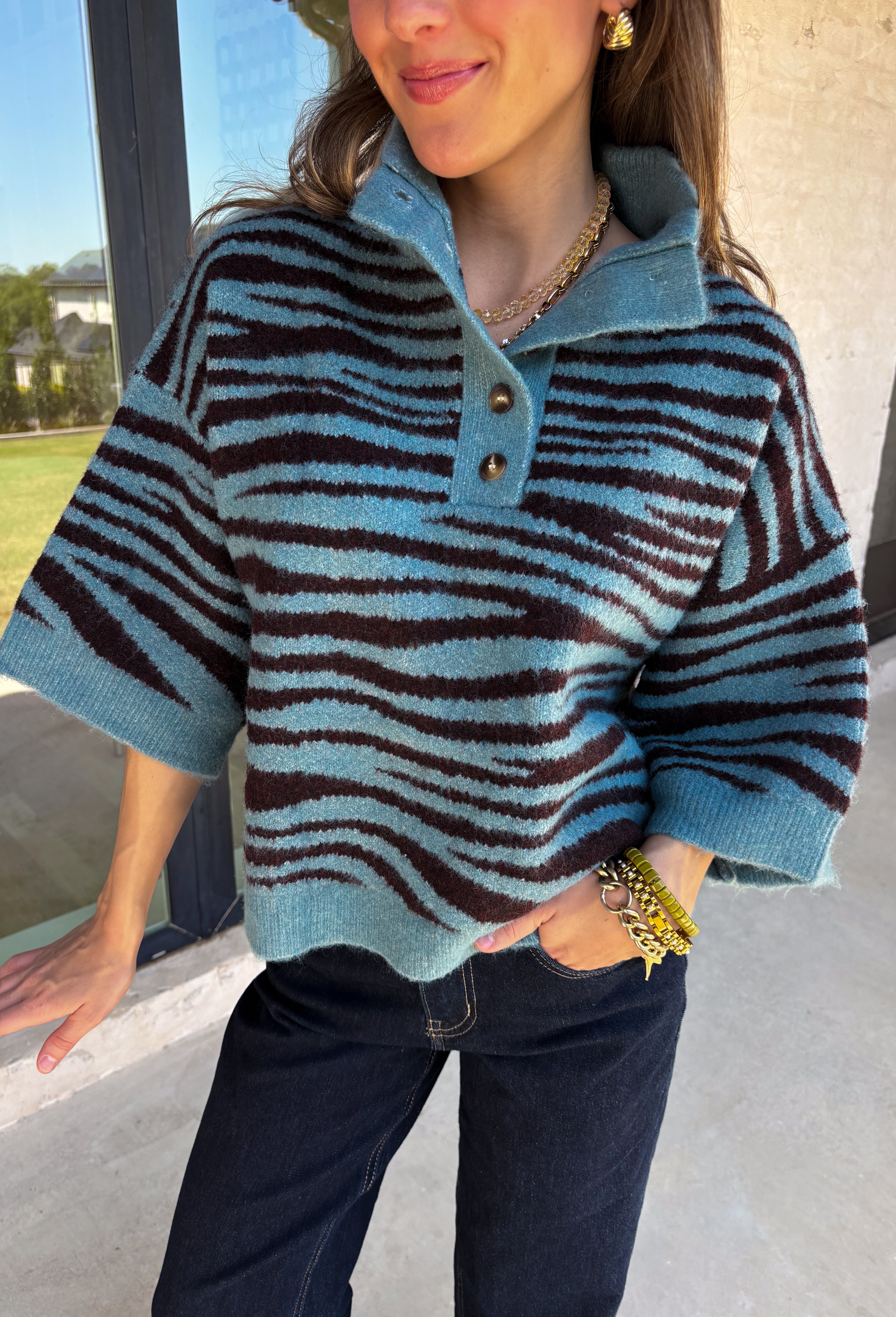 A dusty blue background gives this cozy knit sweater from Entro a fresh pop of color for the season. The darker abstract animal print creates a bold contrast against the dusty blue shade, adding plenty of personality without being difficult to style. A stand neckline and partial button-front closure bring a classic touch to the relaxed knit silhouette, while the ¾ sleeves make it a great option for transitional weather. 
