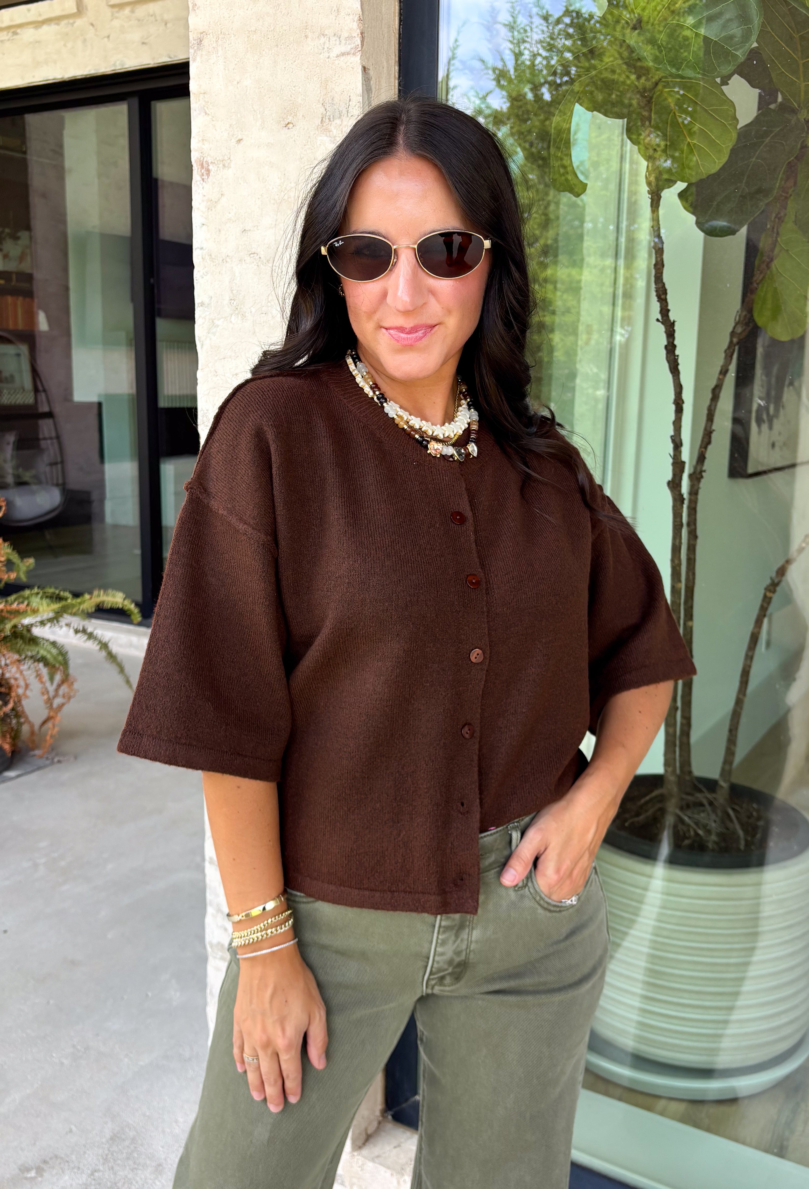 Cozy, classic, and endlessly versatile, this button-down cardigan from Double Zero is the perfect layering piece for the season. Designed in a rich dark brown hue, this soft knit cardigan is easy to style with everything from denim to dresses. The ribbed neckline adds a timeless touch, while the cozy knit construction keeps you comfortable throughout the day. Wear it buttoned as a sweater or open over your favorite basics for an effortlessly polished fall look.