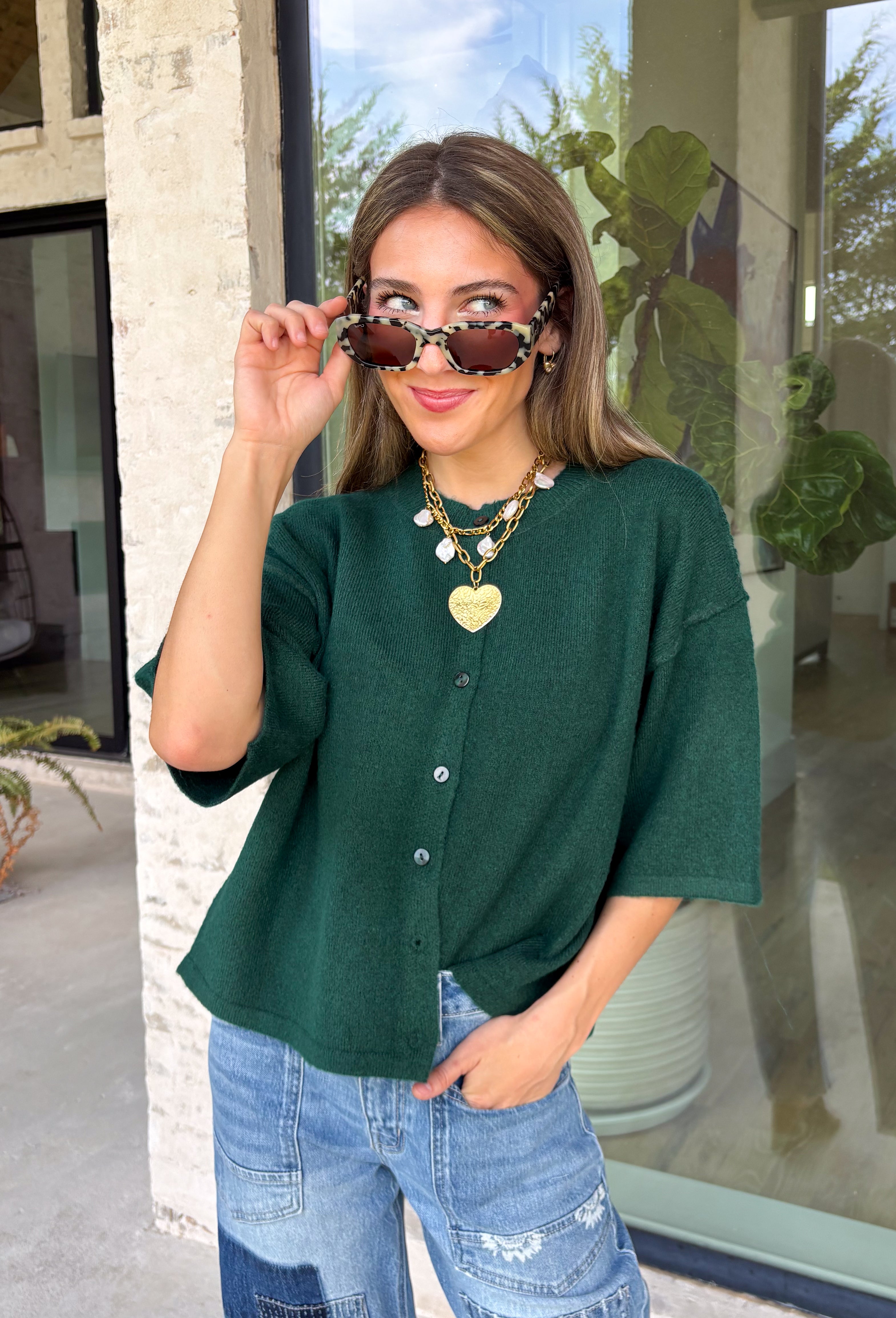 Cozy, classic, and endlessly versatile, this button-down cardigan from Double Zero is the perfect layering piece for the season. Designed in a rich dark green hue, this soft knit cardigan is easy to style with everything from denim to dresses. The ribbed neckline adds a timeless touch, while the cozy knit construction keeps you comfortable throughout the day. Wear it buttoned as a sweater or open over your favorite basics for an effortlessly polished fall look.