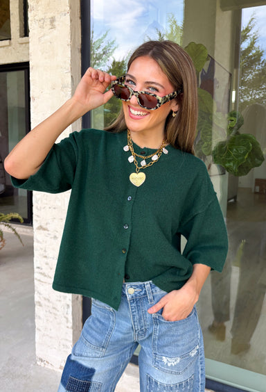 Cozy, classic, and endlessly versatile, this button-down cardigan from Double Zero is the perfect layering piece for the season. Designed in a rich dark green hue, this soft knit cardigan is easy to style with everything from denim to dresses. The ribbed neckline adds a timeless touch, while the cozy knit construction keeps you comfortable throughout the day. Wear it buttoned as a sweater or open over your favorite basics for an effortlessly polished fall look.