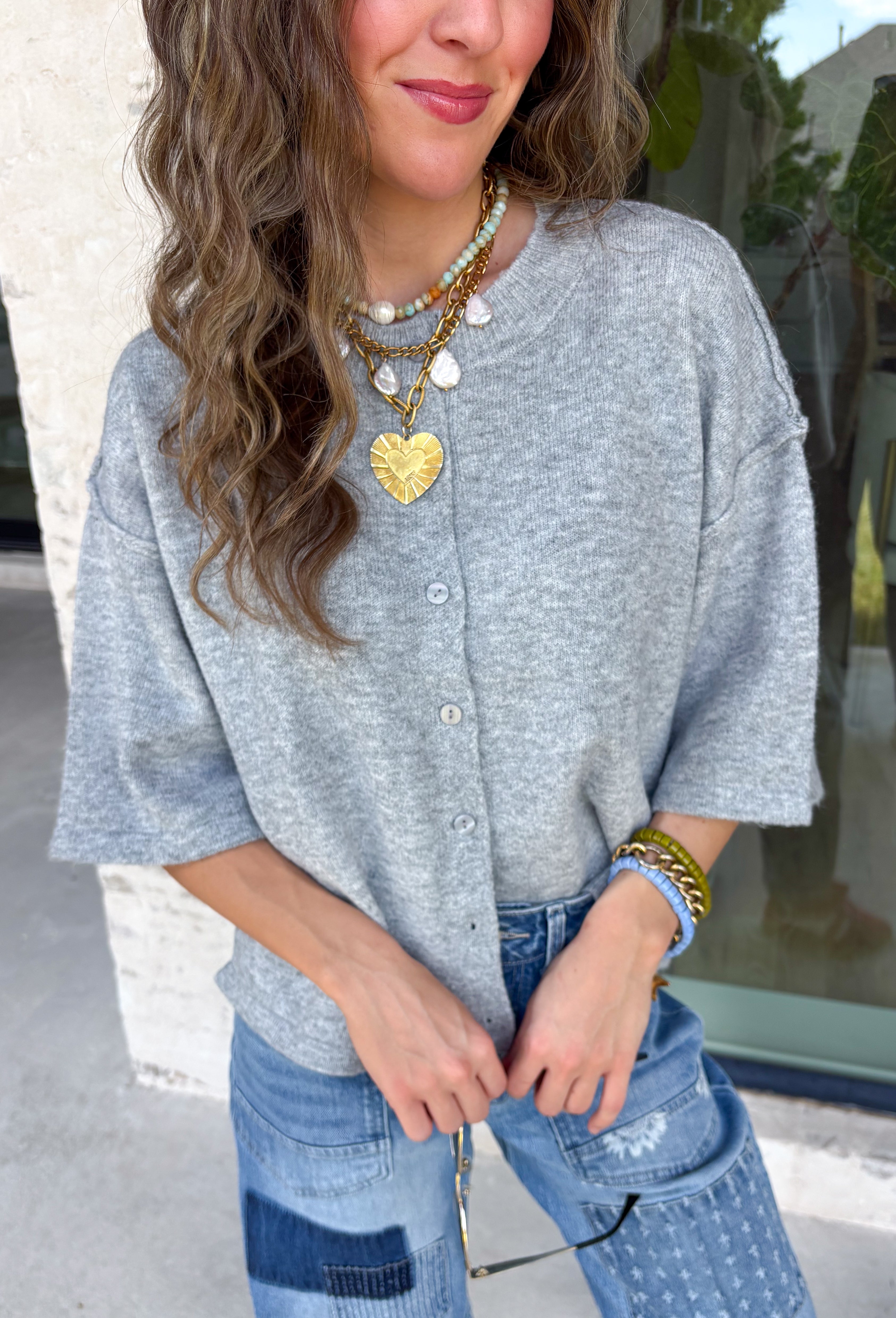 Cozy, classic, and endlessly versatile, this button-down cardigan from Double Zero is the perfect layering piece for the season. Designed in a heather grey hue, this soft knit cardigan is easy to style with everything from denim to dresses. The ribbed neckline adds a timeless touch, while the cozy knit construction keeps you comfortable throughout the day. Wear it buttoned as a sweater or open over your favorite basics for an effortlessly polished fall look.