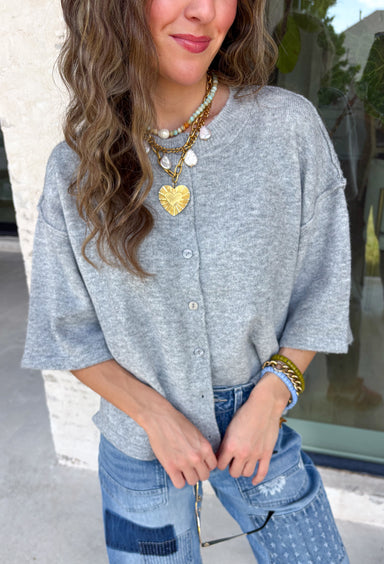 Cozy, classic, and endlessly versatile, this button-down cardigan from Double Zero is the perfect layering piece for the season. Designed in a heather grey hue, this soft knit cardigan is easy to style with everything from denim to dresses. The ribbed neckline adds a timeless touch, while the cozy knit construction keeps you comfortable throughout the day. Wear it buttoned as a sweater or open over your favorite basics for an effortlessly polished fall look.