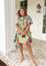 Bright, cheerful, and full of spring charm, this off-white short sleeve dress by Entro is an instant mood booster. Featuring a colorful floral print with pops of green, blue, red, and pink, it feels lively yet easy to wear. The ruffle neckline, ruffle sleeves, and ruffle trim down the front add a soft, feminine touch, while the pleating detail and front button accents give it a polished finish. 