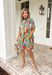 Bright, cheerful, and full of spring charm, this off-white short sleeve dress by Entro is an instant mood booster. Featuring a colorful floral print with pops of green, blue, red, and pink, it feels lively yet easy to wear. The ruffle neckline, ruffle sleeves, and ruffle trim down the front add a soft, feminine touch, while the pleating detail and front button accents give it a polished finish. 