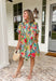 Bright, cheerful, and full of spring charm, this off-white short sleeve dress by Entro is an instant mood booster. Featuring a colorful floral print with pops of green, blue, red, and pink, it feels lively yet easy to wear. The ruffle neckline, ruffle sleeves, and ruffle trim down the front add a soft, feminine touch, while the pleating detail and front button accents give it a polished finish. 