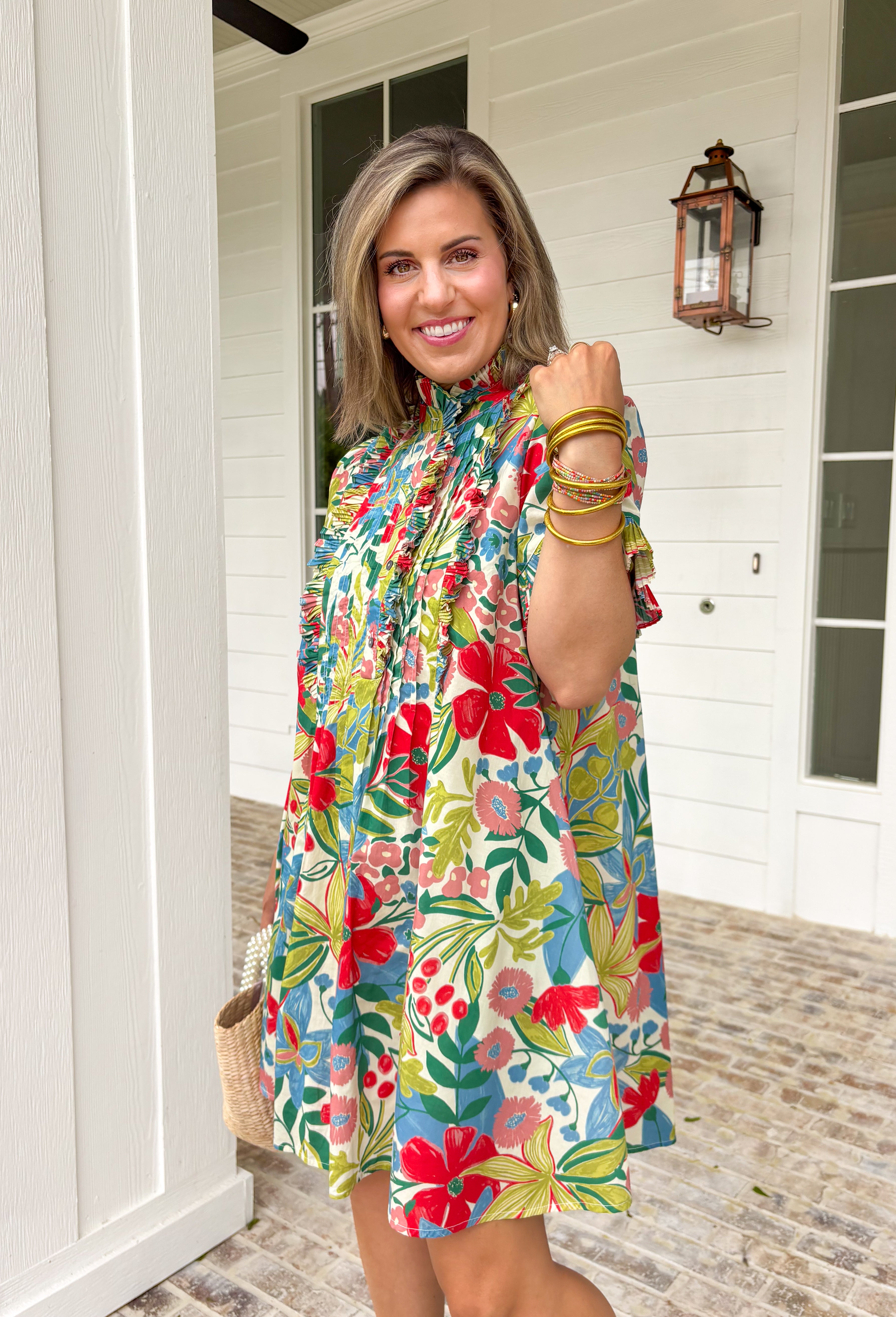 Bright, cheerful, and full of spring charm, this off-white short sleeve dress by Entro is an instant mood booster. Featuring a colorful floral print with pops of green, blue, red, and pink, it feels lively yet easy to wear. The ruffle neckline, ruffle sleeves, and ruffle trim down the front add a soft, feminine touch, while the pleating detail and front button accents give it a polished finish. 