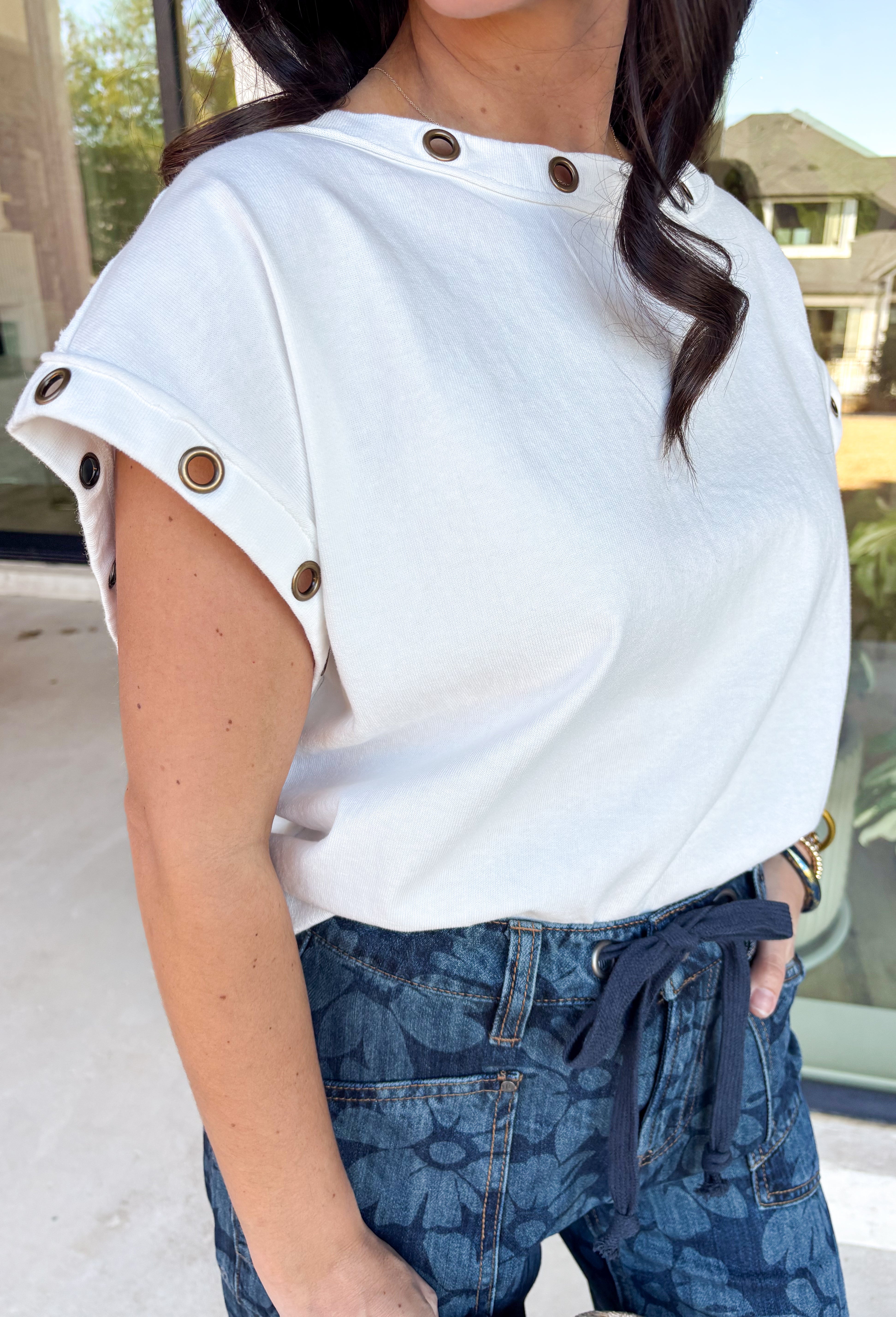 Clean, crisp, with a cool edge—this white short sleeve top by Entro is a fresh spring staple with a twist. Designed with hollow eyelet hardware along the neckline and sleeves, it adds just the right amount of edge to an otherwise classic silhouette. Made from breathable cotton, this top is lightweight, comfortable, and easy to dress up or down for everyday spring wear.