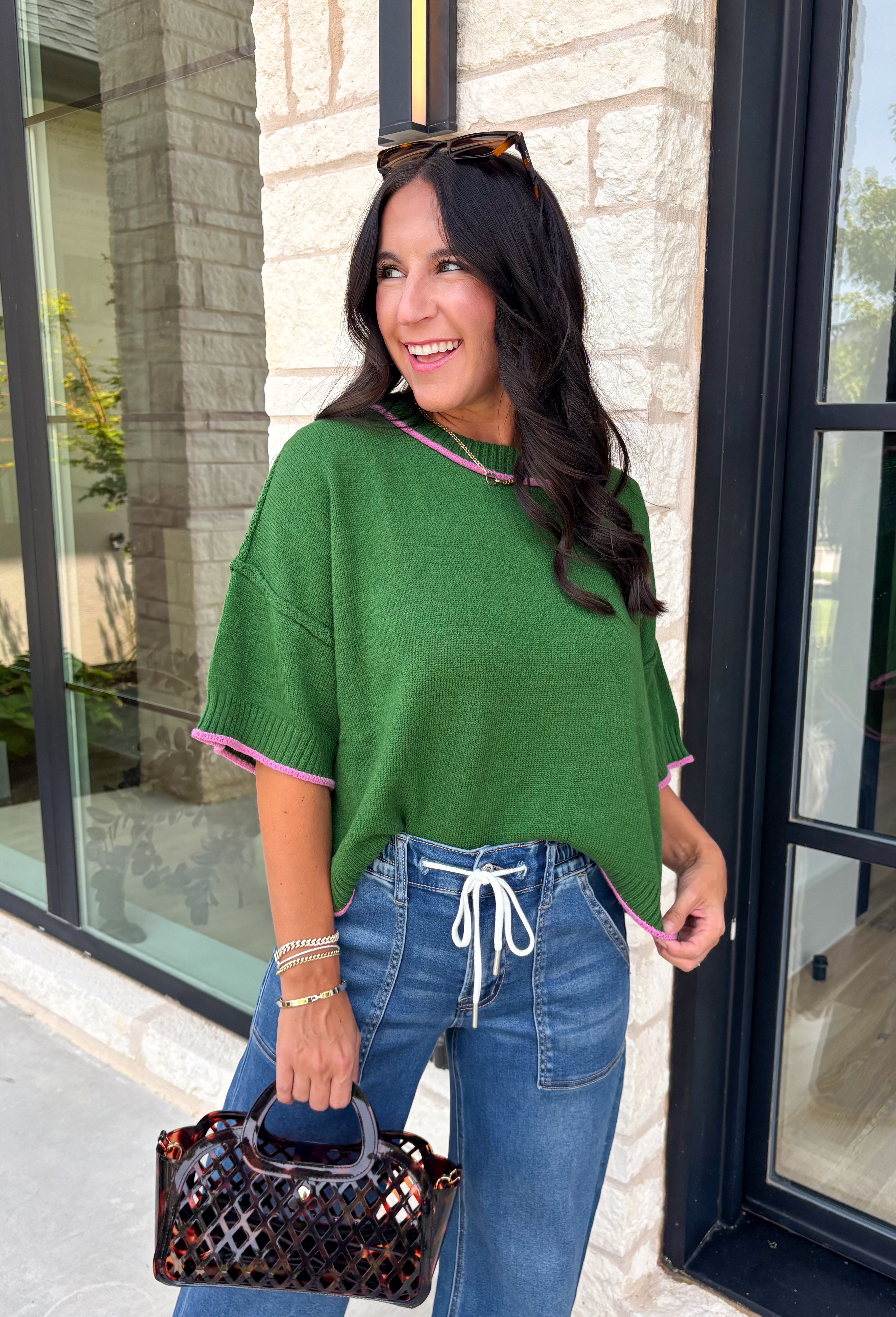 Add a playful pop of color to your fall wardrobe with this cozy short sleeve sweater! Featuring a rich pine green knit with soft pink contrast trim, this sweater is the perfect mix of timeless and fun. The ribbed detailing along the neckline, sleeves, and hem adds a classic finishing touch, while the lightweight knit keeps it comfortable for layering throughout the season. 