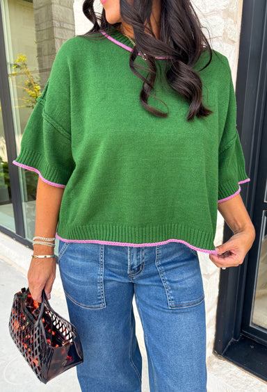 Add a playful pop of color to your fall wardrobe with this cozy short sleeve sweater! Featuring a rich pine green knit with soft pink contrast trim, this sweater is the perfect mix of timeless and fun. The ribbed detailing along the neckline, sleeves, and hem adds a classic finishing touch, while the lightweight knit keeps it comfortable for layering throughout the season. 
