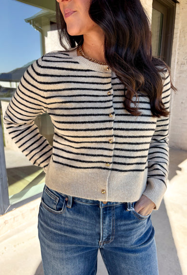 Chic, cozy, and perfect for winter layering, this taupe button-down cardigan by Paper Moon brings a modern twist to a classic stripe. Featuring black stripe detailing and gleaming gold buttons, this cropped knit adds just the right amount of polish to your cold-weather wardrobe. Soft, warm, and easy to style, it’s the ideal piece for dressing up denim or layering over your favorite winter basics.