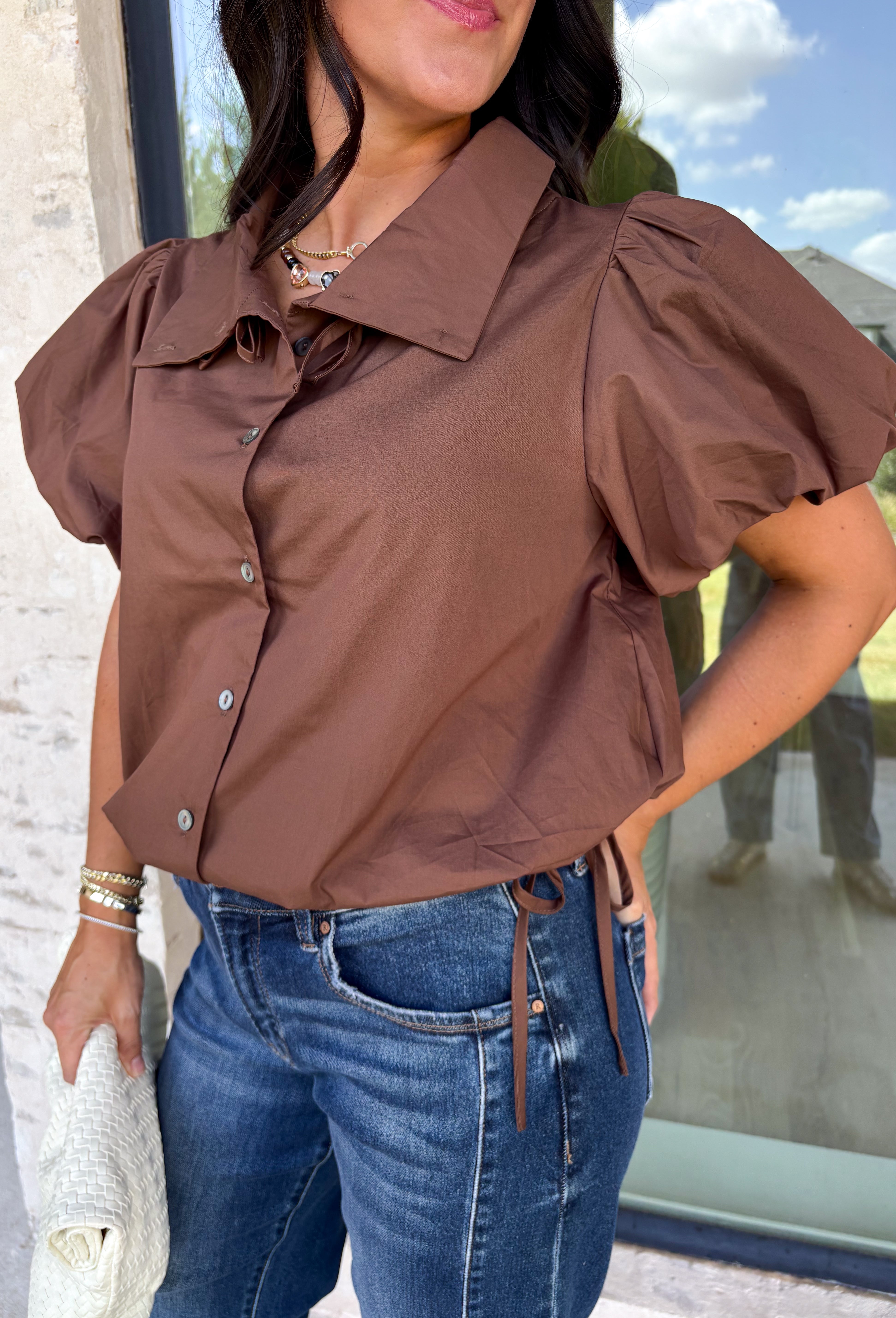 Elevate your everyday wardrobe with this effortlessly polished blouse from Entro. Designed in a rich chocolate brown hue, this timeless top features a classic button-front design with a collared neckline for a sophisticated look. Feminine puff sleeves and charming side tie details add a modern twist, creating a flattering silhouette that's easy to dress up or down. Crafted from breathable cotton, this versatile blouse is perfect for everything from office days to weekend brunches.