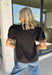 Elevate your everyday wardrobe with this effortlessly polished top from Entro. Designed in a classic black hue, this versatile blouse features beautiful tan and cream contrast binding along the flattering v-neckline for a sophisticated touch. The nonfunctional button detail at the front adds timeless charm, while the short puff sleeves with contrast cuffs create a feminine silhouette. Easy to dress up or down, this top is perfect for workdays, dinner dates, and everything in between.