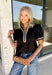Elevate your everyday wardrobe with this effortlessly polished top from Entro. Designed in a classic black hue, this versatile blouse features beautiful tan and cream contrast binding along the flattering v-neckline for a sophisticated touch. The nonfunctional button detail at the front adds timeless charm, while the short puff sleeves with contrast cuffs create a feminine silhouette. Easy to dress up or down, this top is perfect for workdays, dinner dates, and everything in between.