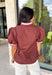 Elevate your everyday wardrobe with this effortlessly polished top from Entro. Designed in a classic chocolate hue, this versatile blouse features beautiful pink and cream contrast binding along the flattering v-neckline for a sophisticated touch. The nonfunctional button detail at the front adds timeless charm, while the short puff sleeves with contrast cuffs create a feminine silhouette. Easy to dress up or down, this top is perfect for workdays, dinner dates, and everything in between.