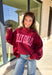 Make your winter wardrobe a little more fun with this playful “Dilly Dally” pullover by Bucket List. Featuring bold hot pink lettering on a rich burgundy backdrop, this cozy mock neck sweatshirt is made for chill days and cheerful moods. With its oversized fit and soft fabric, it’s the perfect mix of comfort and attitude for the season.