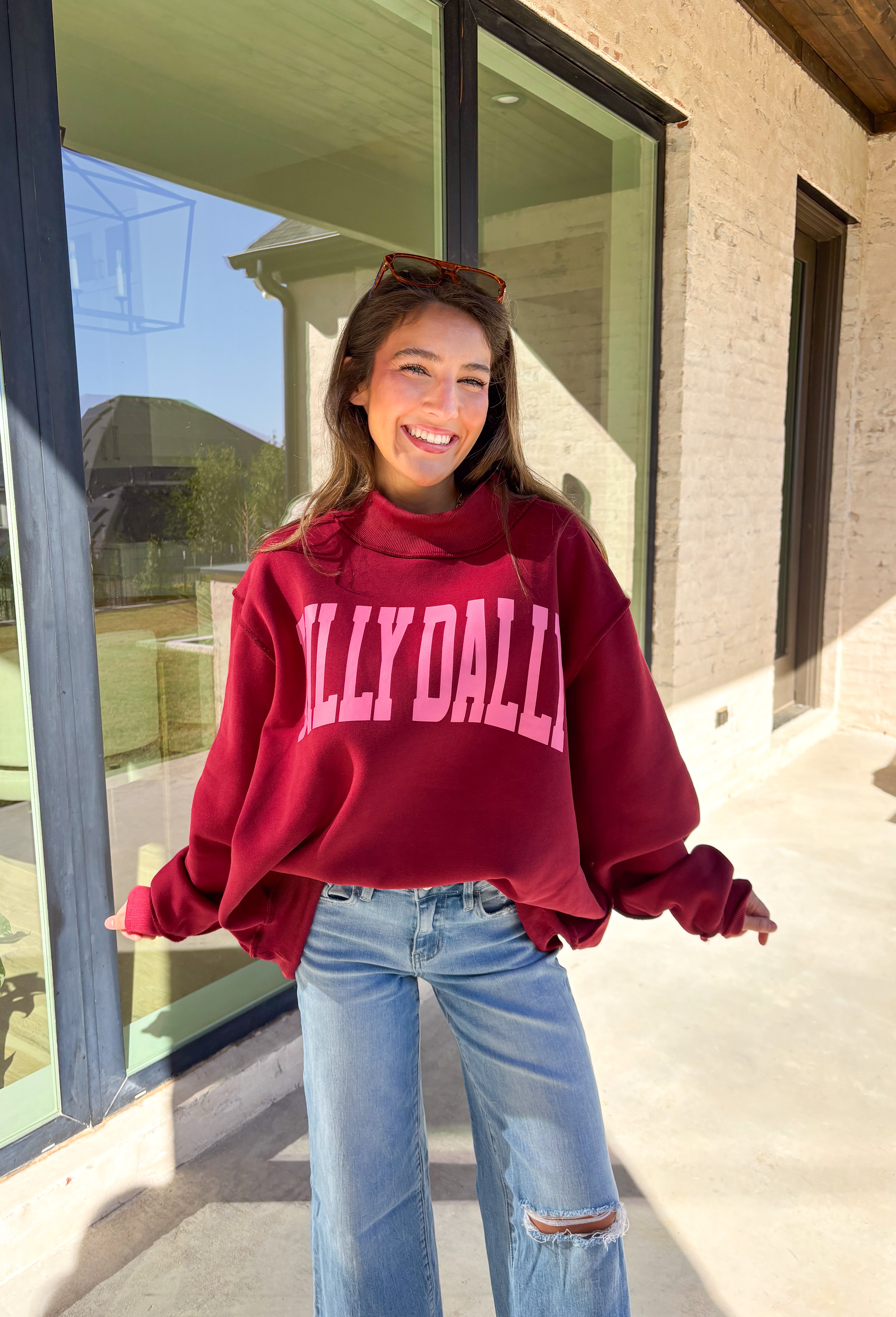 Make your winter wardrobe a little more fun with this playful “Dilly Dally” pullover by Bucket List. Featuring bold hot pink lettering on a rich burgundy backdrop, this cozy mock neck sweatshirt is made for chill days and cheerful moods. With its oversized fit and soft fabric, it’s the perfect mix of comfort and attitude for the season.