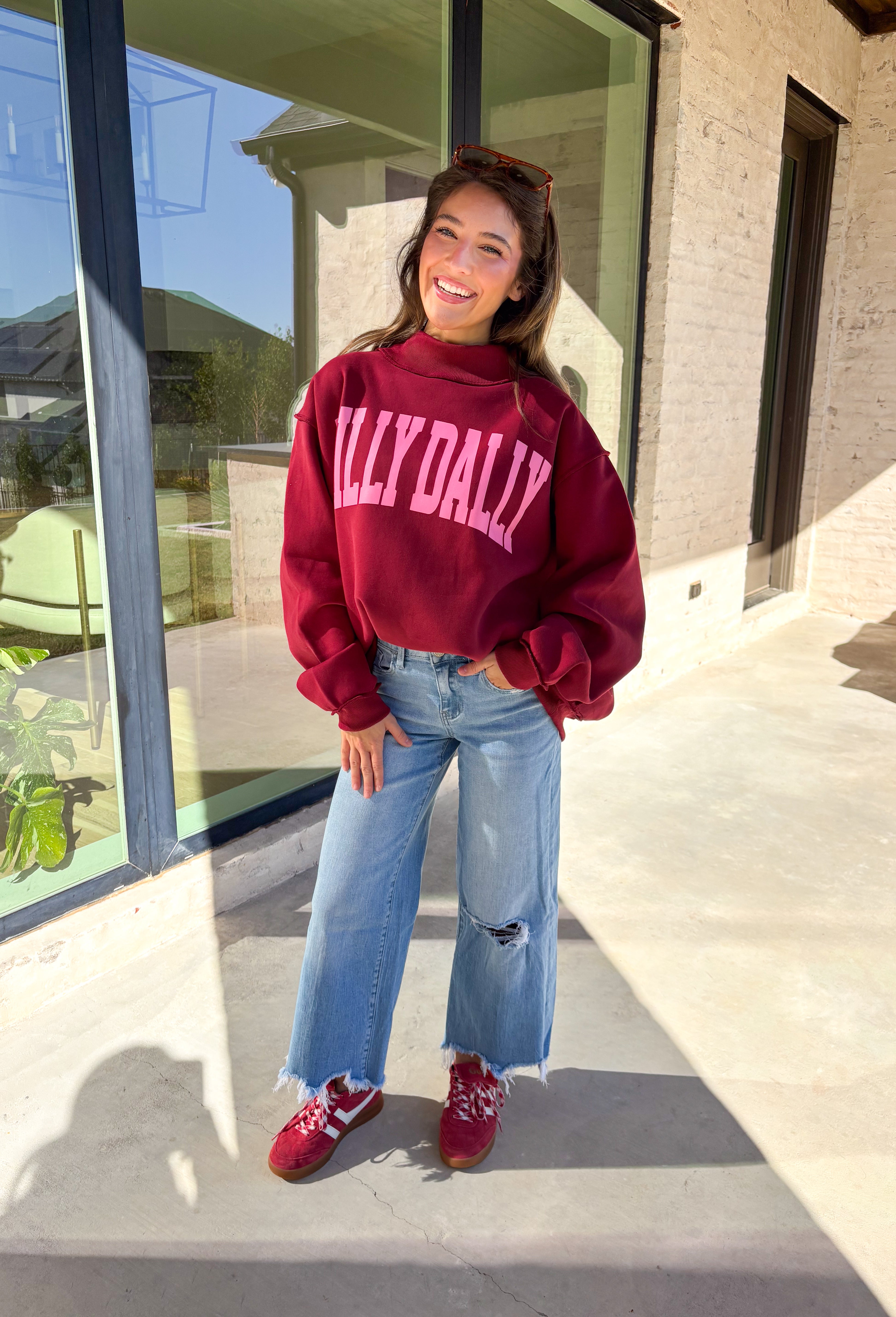 Make your winter wardrobe a little more fun with this playful “Dilly Dally” pullover by Bucket List. Featuring bold hot pink lettering on a rich burgundy backdrop, this cozy mock neck sweatshirt is made for chill days and cheerful moods. With its oversized fit and soft fabric, it’s the perfect mix of comfort and attitude for the season.