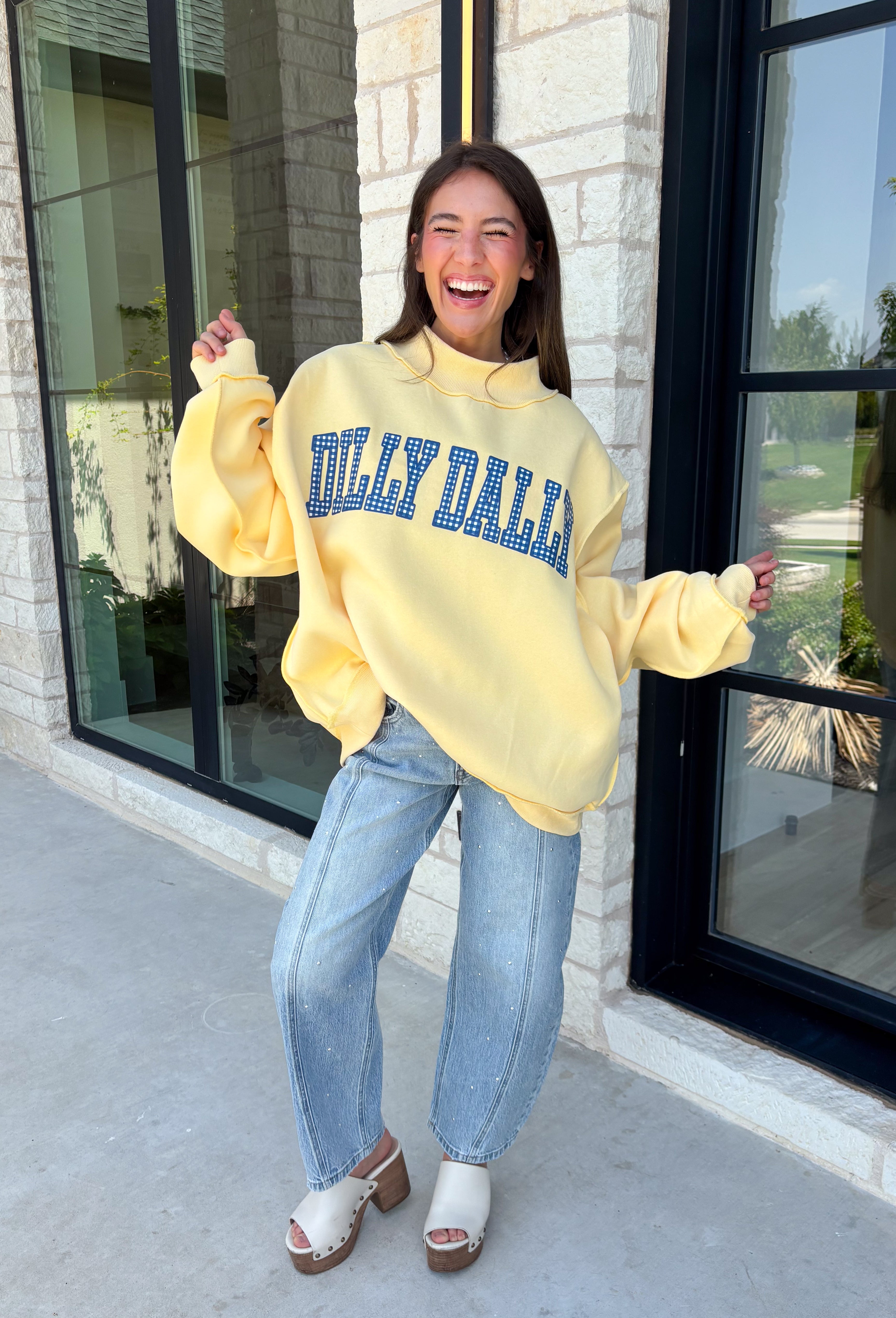 Why choose one look when you can have two? This cozy reversible pullover is full of personality with playful sayings on each side. One side features "Dilly Dally" in blue and white gingham lettering, while the fleece-lined reverse showcases "Lolly Gag" in pink and white gingham for an equally fun look. Designed with an oversized fit and a classic mock neckline, this butter yellow sweatshirt is perfect for slow mornings, coffee runs, travel days, and all your cozy fall adventures.