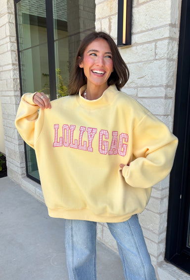 Why choose one look when you can have two? This cozy reversible pullover is full of personality with playful sayings on each side. One side features "Dilly Dally" in blue and white gingham lettering, while the fleece-lined reverse showcases "Lolly Gag" in pink and white gingham for an equally fun look. Designed with an oversized fit and a classic mock neckline, this butter yellow sweatshirt is perfect for slow mornings, coffee runs, travel days, and all your cozy fall adventures.
