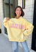 Why choose one look when you can have two? This cozy reversible pullover is full of personality with playful sayings on each side. One side features "Dilly Dally" in blue and white gingham lettering, while the fleece-lined reverse showcases "Lolly Gag" in pink and white gingham for an equally fun look. Designed with an oversized fit and a classic mock neckline, this butter yellow sweatshirt is perfect for slow mornings, coffee runs, travel days, and all your cozy fall adventures.