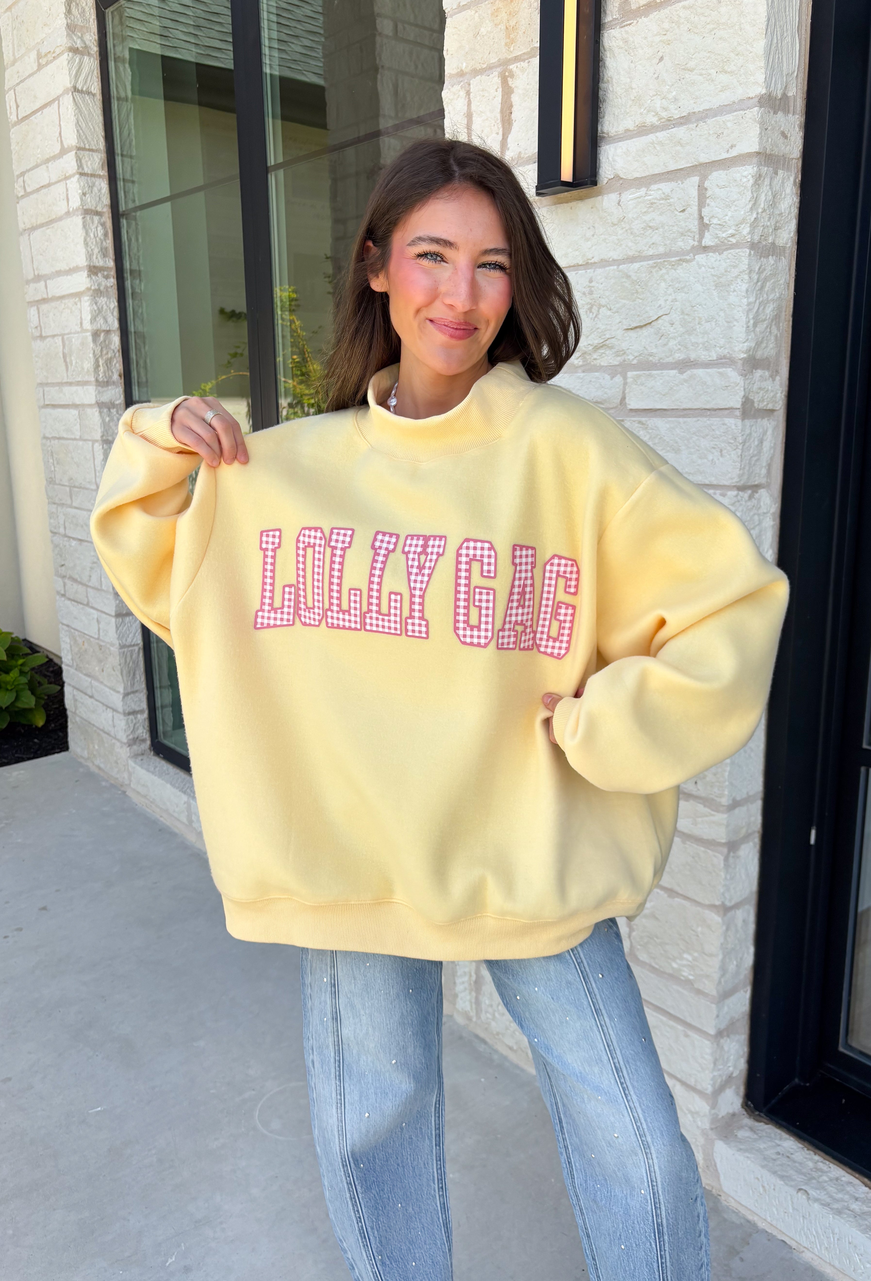 Why choose one look when you can have two? This cozy reversible pullover is full of personality with playful sayings on each side. One side features "Dilly Dally" in blue and white gingham lettering, while the fleece-lined reverse showcases "Lolly Gag" in pink and white gingham for an equally fun look. Designed with an oversized fit and a classic mock neckline, this butter yellow sweatshirt is perfect for slow mornings, coffee runs, travel days, and all your cozy fall adventures.