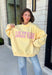 Why choose one look when you can have two? This cozy reversible pullover is full of personality with playful sayings on each side. One side features "Dilly Dally" in blue and white gingham lettering, while the fleece-lined reverse showcases "Lolly Gag" in pink and white gingham for an equally fun look. Designed with an oversized fit and a classic mock neckline, this butter yellow sweatshirt is perfect for slow mornings, coffee runs, travel days, and all your cozy fall adventures.