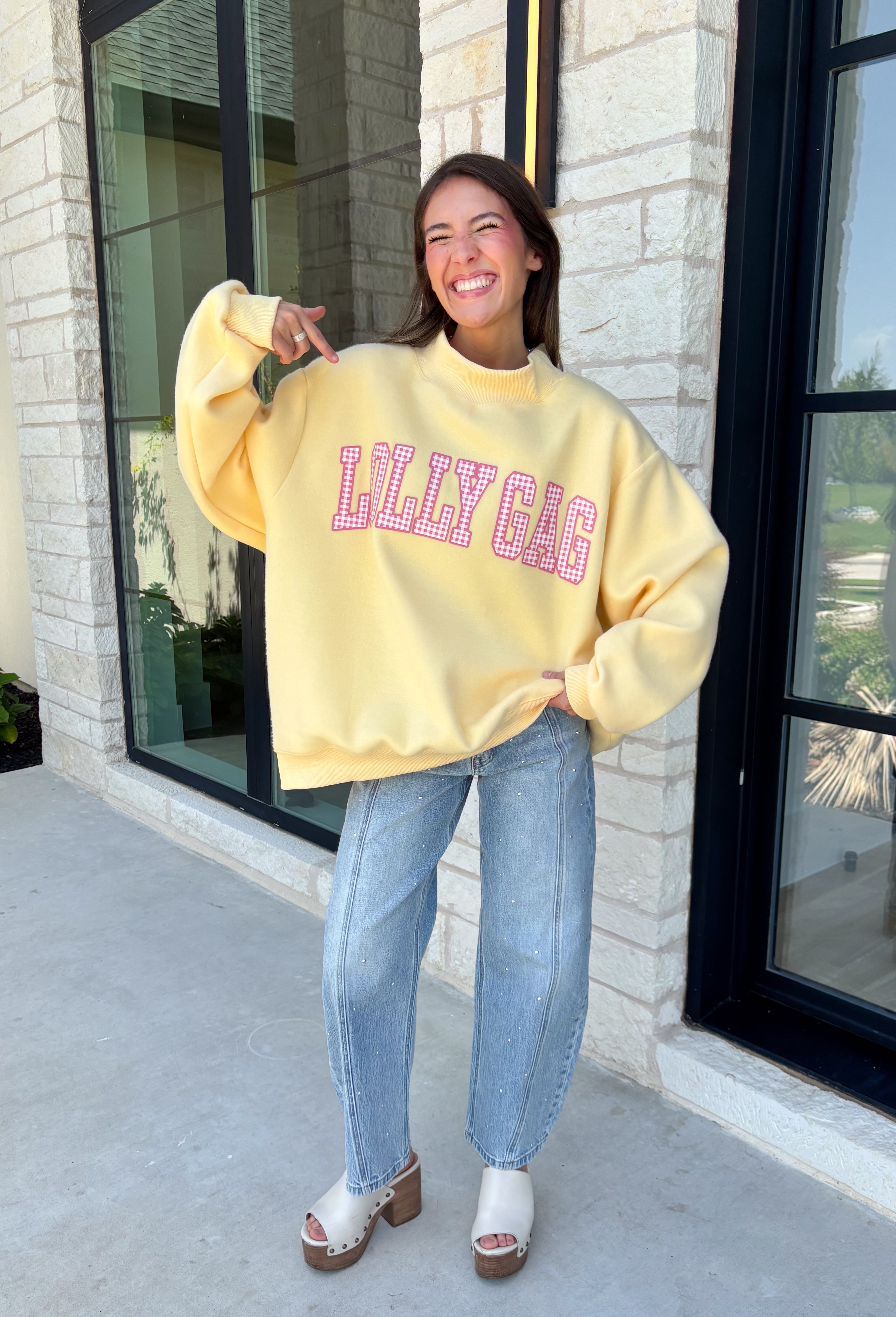 Why choose one look when you can have two? This cozy reversible pullover is full of personality with playful sayings on each side. One side features "Dilly Dally" in blue and white gingham lettering, while the fleece-lined reverse showcases "Lolly Gag" in pink and white gingham for an equally fun look. Designed with an oversized fit and a classic mock neckline, this butter yellow sweatshirt is perfect for slow mornings, coffee runs, travel days, and all your cozy fall adventures.