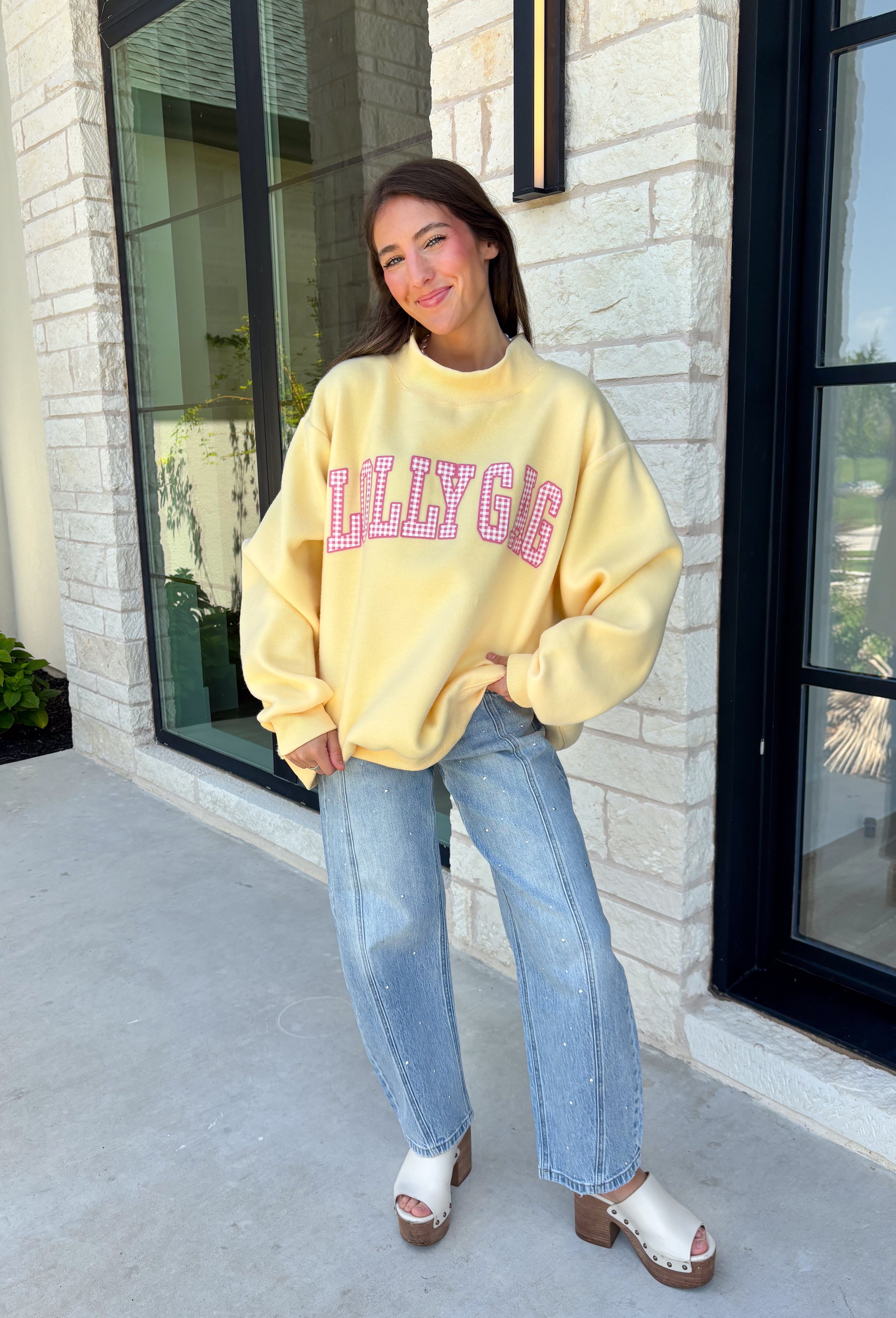 Why choose one look when you can have two? This cozy reversible pullover is full of personality with playful sayings on each side. One side features "Dilly Dally" in blue and white gingham lettering, while the fleece-lined reverse showcases "Lolly Gag" in pink and white gingham for an equally fun look. Designed with an oversized fit and a classic mock neckline, this butter yellow sweatshirt is perfect for slow mornings, coffee runs, travel days, and all your cozy fall adventures.