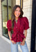 Rich seasonal color and flattering details make this merlot blouse a must-have for fall! Crafted from breathable cotton, this feminine top features a button front, soft puff sleeves, and a flattering tie waist that beautifully defines your silhouette. Pleating at the waist adds a polished touch, while the smocked back provides all-day comfort and the perfect fit. 