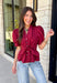Rich seasonal color and flattering details make this merlot blouse a must-have for fall! Crafted from breathable cotton, this feminine top features a button front, soft puff sleeves, and a flattering tie waist that beautifully defines your silhouette. Pleating at the waist adds a polished touch, while the smocked back provides all-day comfort and the perfect fit. 