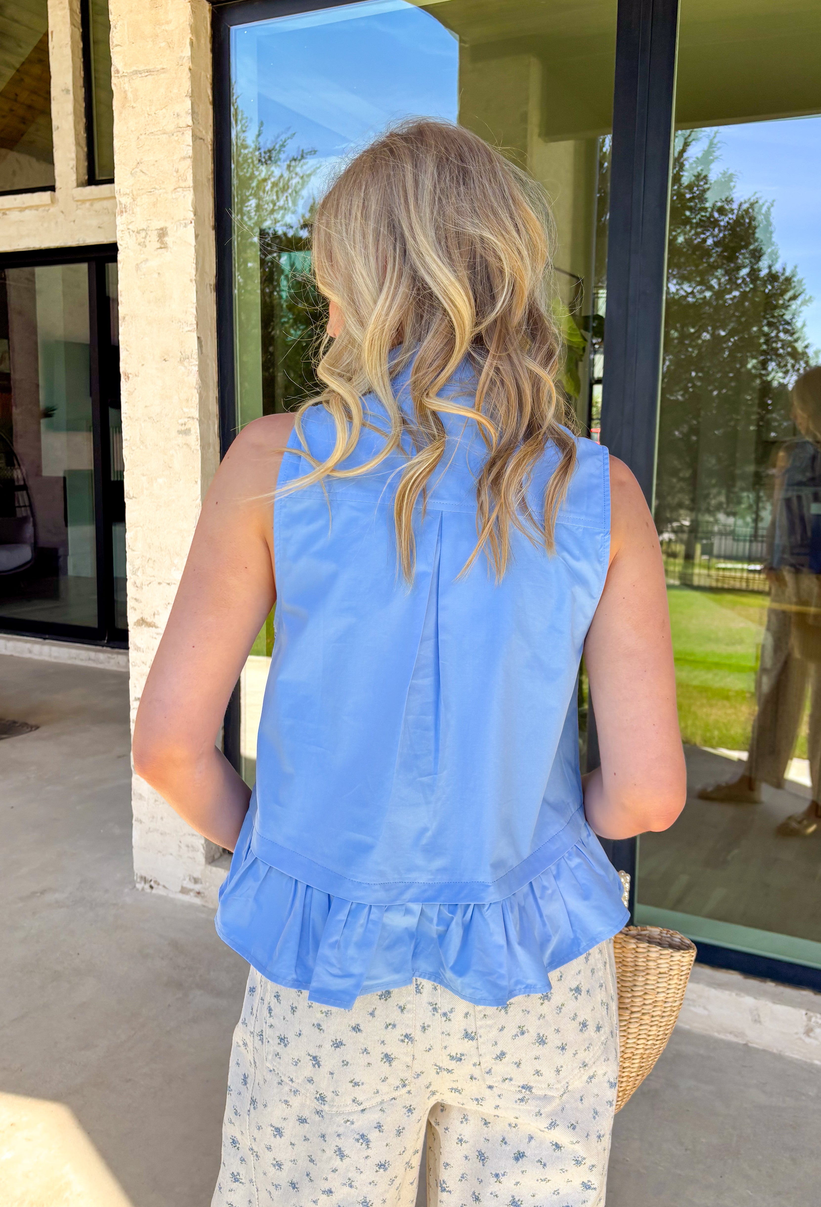 Crisp, classic, and endlessly versatile — this chambray sleeveless button down top is one you’ll reach for again and again. The clean silhouette keeps it timeless, while the tie detail at the top adds a soft, feminine touch that sets it apart from your basic button downs. Finished with a subtle ruffle hem for a hint of movement and charm, this top is lightweight and breathable in 100% cotton. It’s polished enough for work and easy enough for weekend wear — the kind of staple that works all season long.