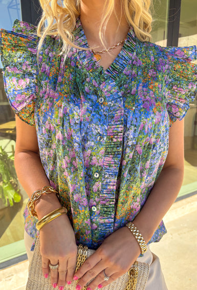 Bright, cheerful, and full of spring charm, this pretty blue short sleeve top by Entro is an instant favorite. Featuring a colorful floral print with pops of green, purple, orange, and yellow, it brings a fun burst of color to your everyday look. The button-down front is accented with pleated trim and soft pleating along the front for a flattering drape, while the pleated ruffle sleeves add the sweetest feminine finish. Made from breathable cotton, this top is perfect for sunny days, brunch plans, and every