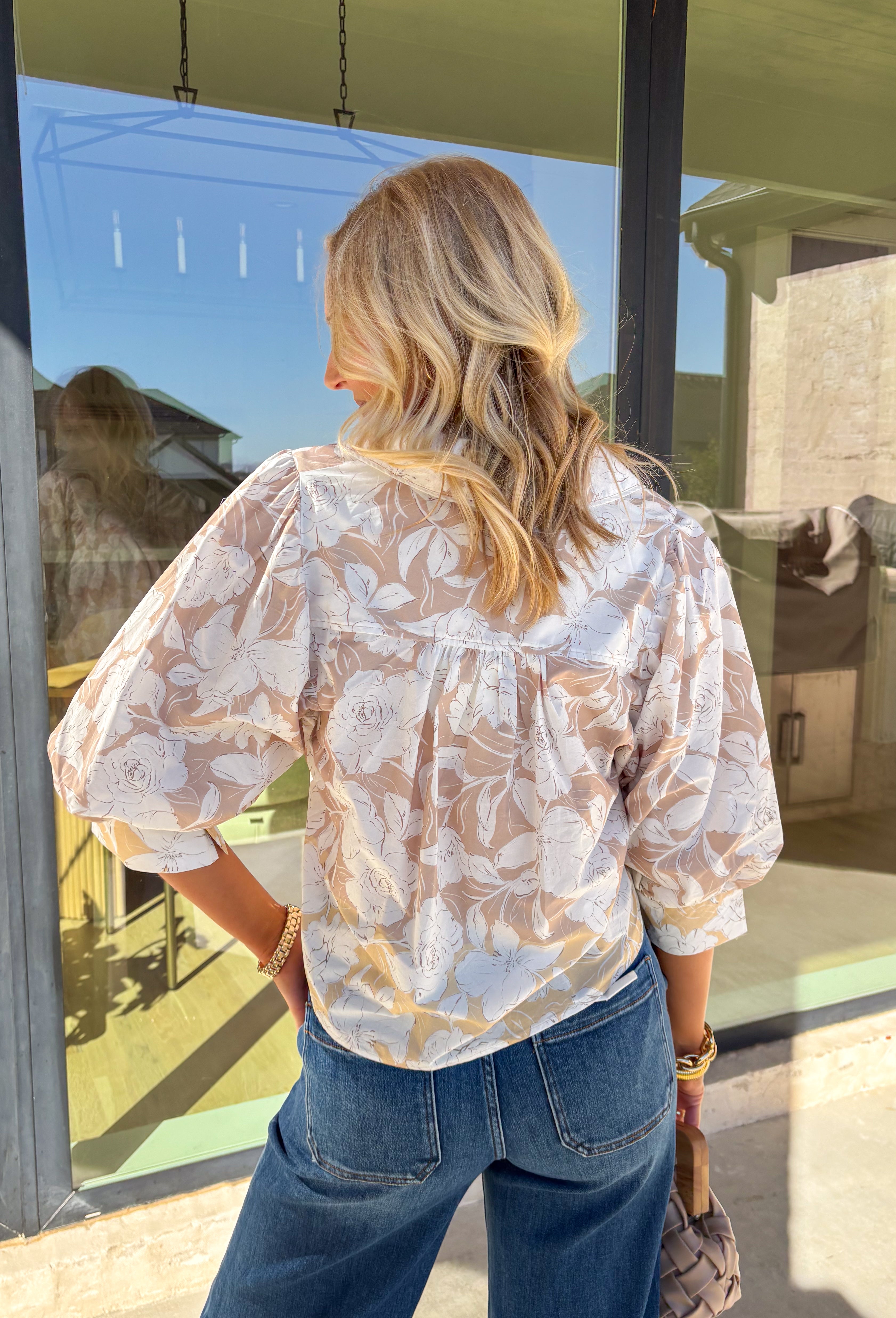 Soft, classic, and perfect for spring, this tan 3/4 sleeve top by Entro is an effortless everyday favorite. Featuring a delicate white floral print throughout, it brings a light, feminine touch to a neutral base. Light peach trim along the hem and sleeve cuffs adds a clean contrast detail, while the collared neckline gives it a polished finish. Made from breathable cotton, this top is easy to wear from workdays to weekend plans.