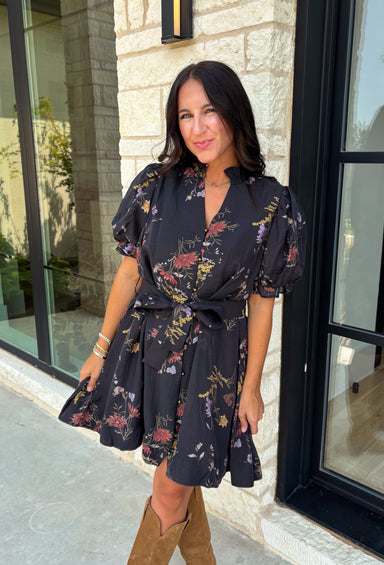Embrace the beauty of the season in this effortlessly feminine floral dress that's made for all your favorite fall occasions. Designed with a classic black backdrop and adorned with a rich floral print in gorgeous autumn-inspired hues, this dress is the perfect combination of timeless elegance and everyday comfort. The ruffled v-neckline and puff sleeves add a romantic touch, while the self-tie waist creates a flattering silhouette you'll love. 