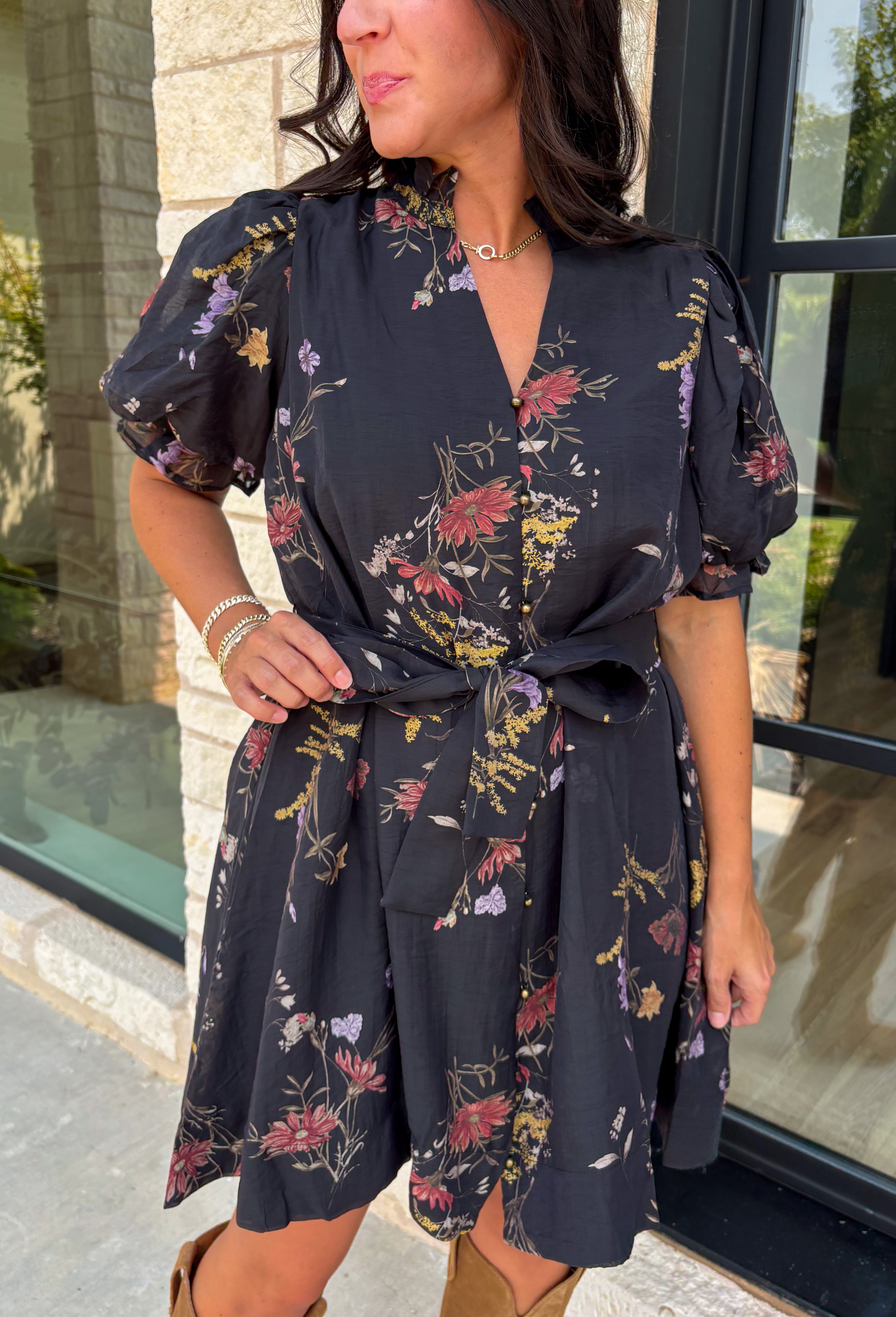 Embrace the beauty of the season in this effortlessly feminine floral dress that's made for all your favorite fall occasions. Designed with a classic black backdrop and adorned with a rich floral print in gorgeous autumn-inspired hues, this dress is the perfect combination of timeless elegance and everyday comfort. The ruffled v-neckline and puff sleeves add a romantic touch, while the self-tie waist creates a flattering silhouette you'll love. 